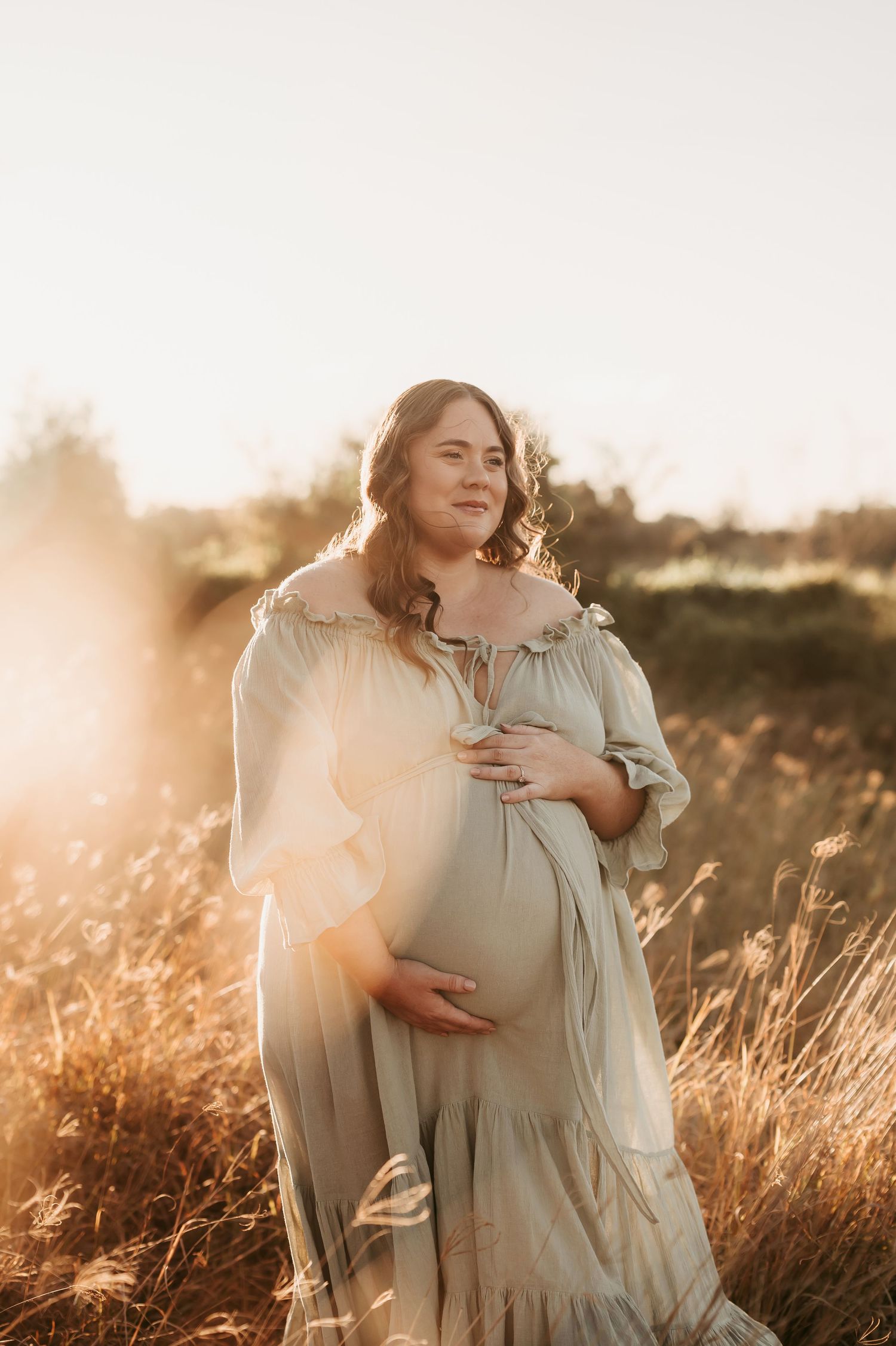 A dreamy maternity photoshoot in a golden field at sunset with flowing white dress and natural lighting.