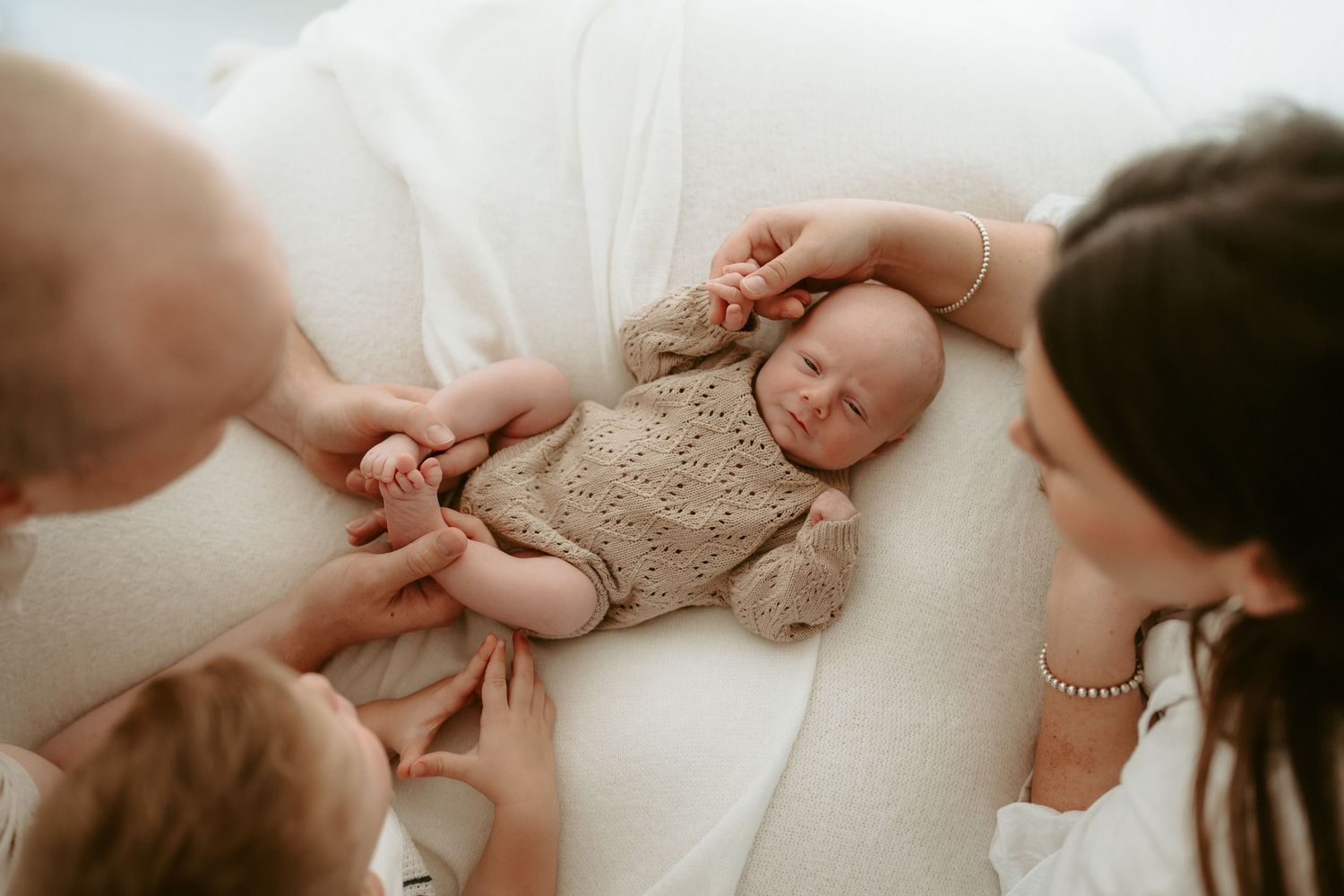 Intimate family photo showing hands tenderly touching newborn baby.