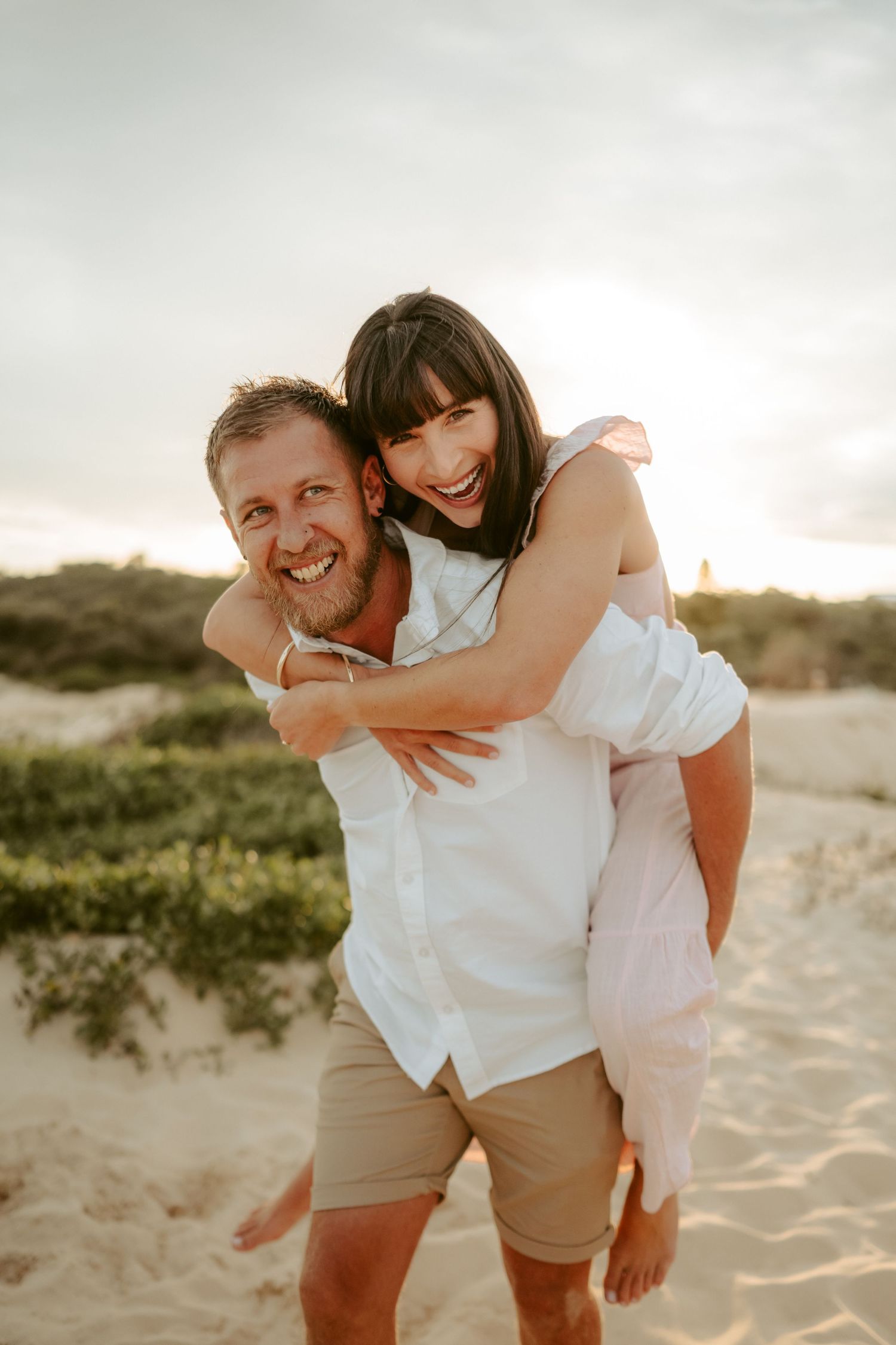 Playful couple enjoying a piggyback ride on a sandy beach at sunset.