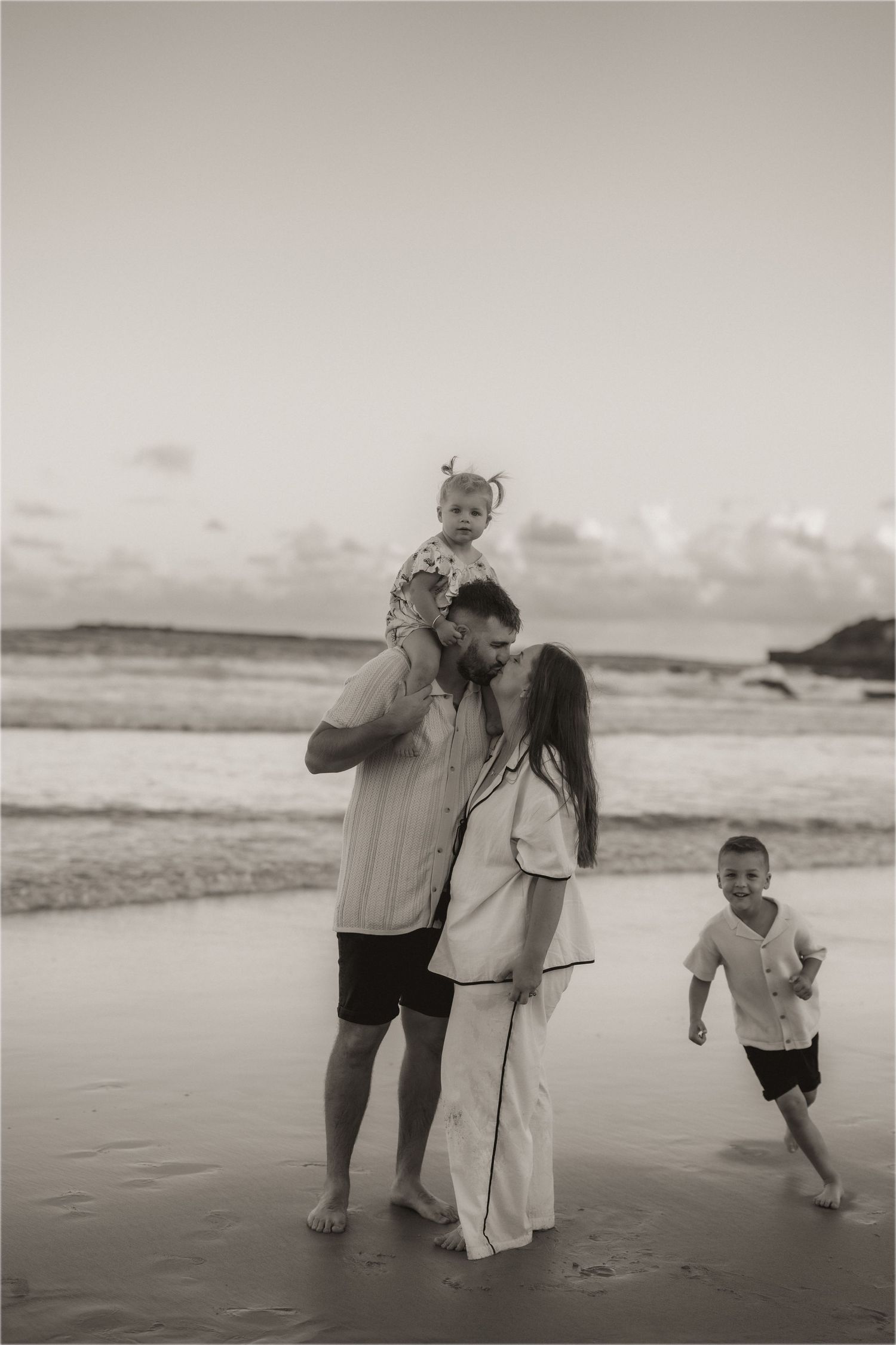 Family enjoying a tender moment together on a beach at sunset in black and white.