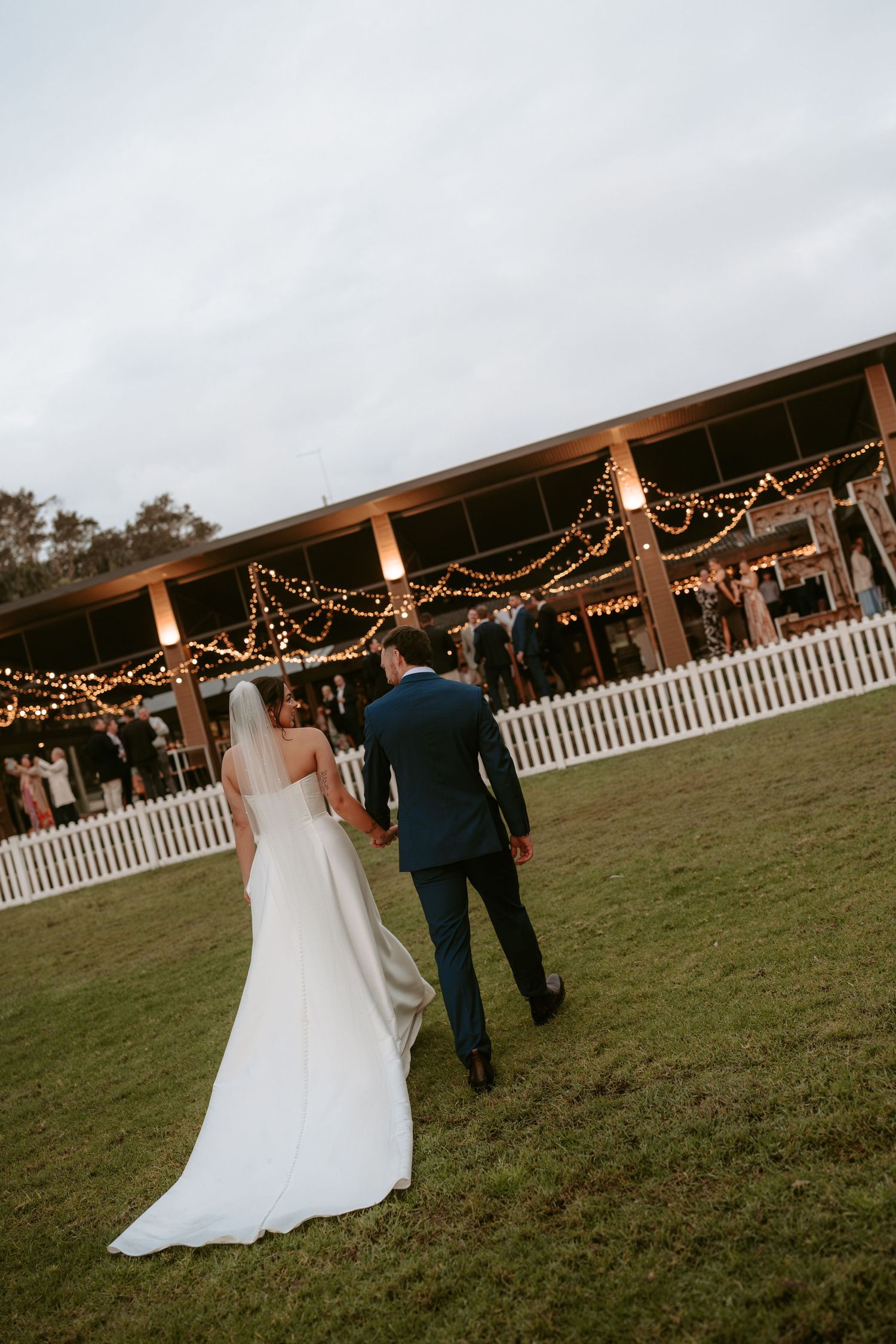 Wedding reception venue with string lights and white picket fence at dusk.