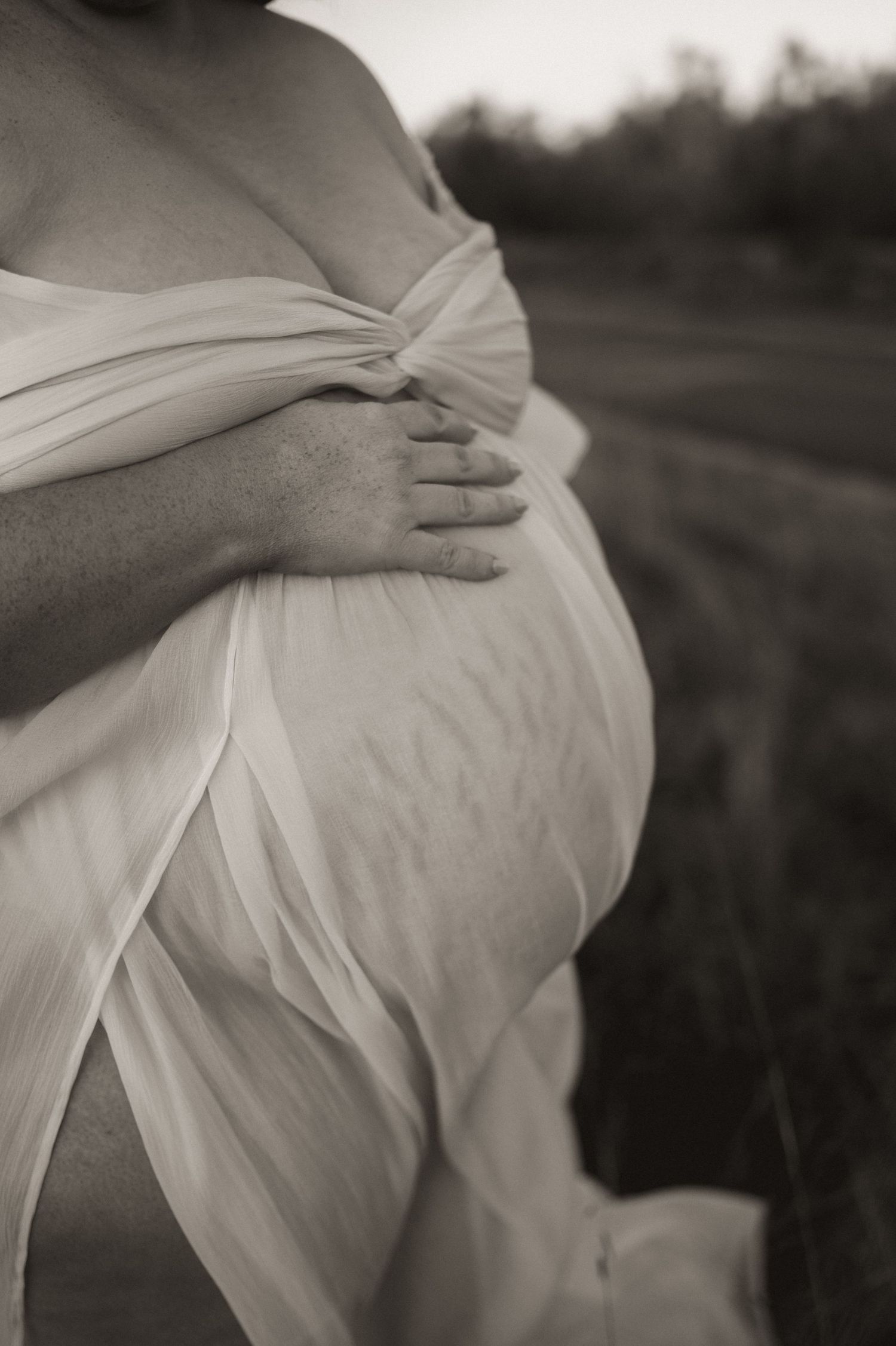 Close-up black and white details of draped white fabric over a pregnant belly.