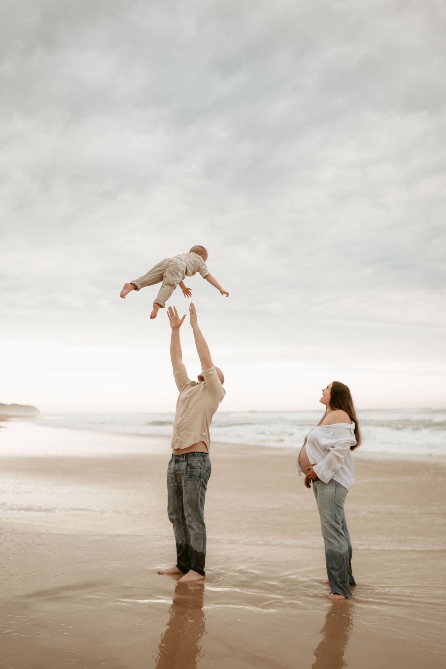 Joyful playtime on a misty beach with people lifting and playing in the sand.
