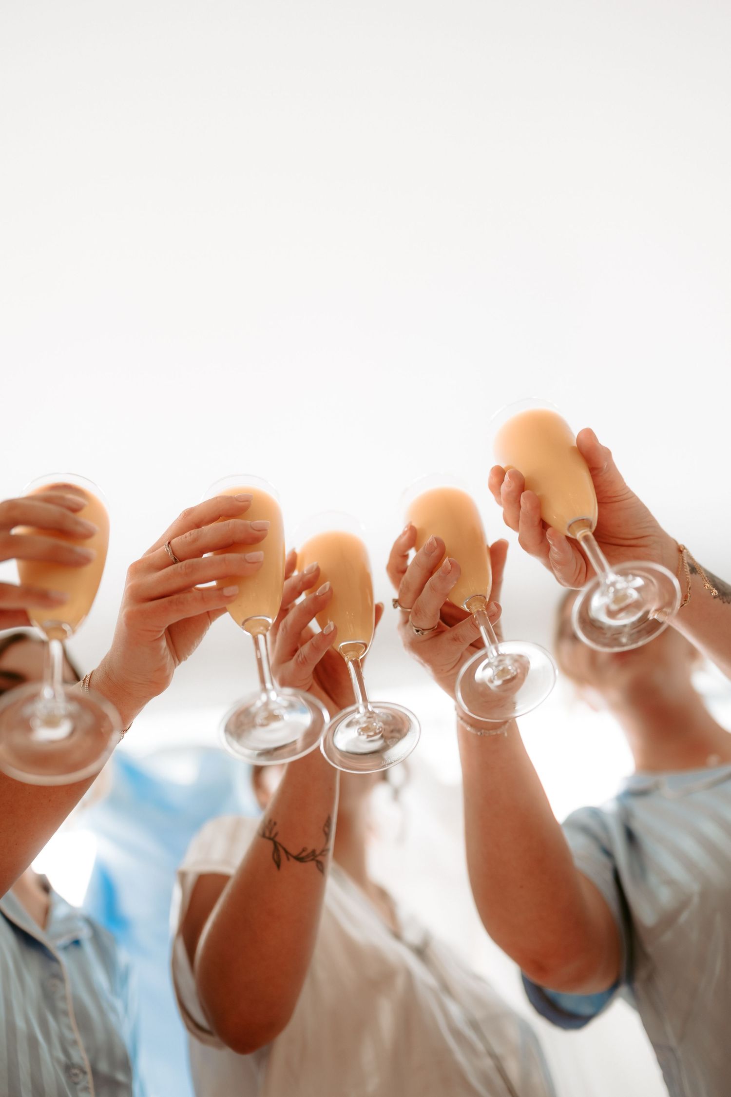 Wedding party raising champagne glasses in celebration against bright background.