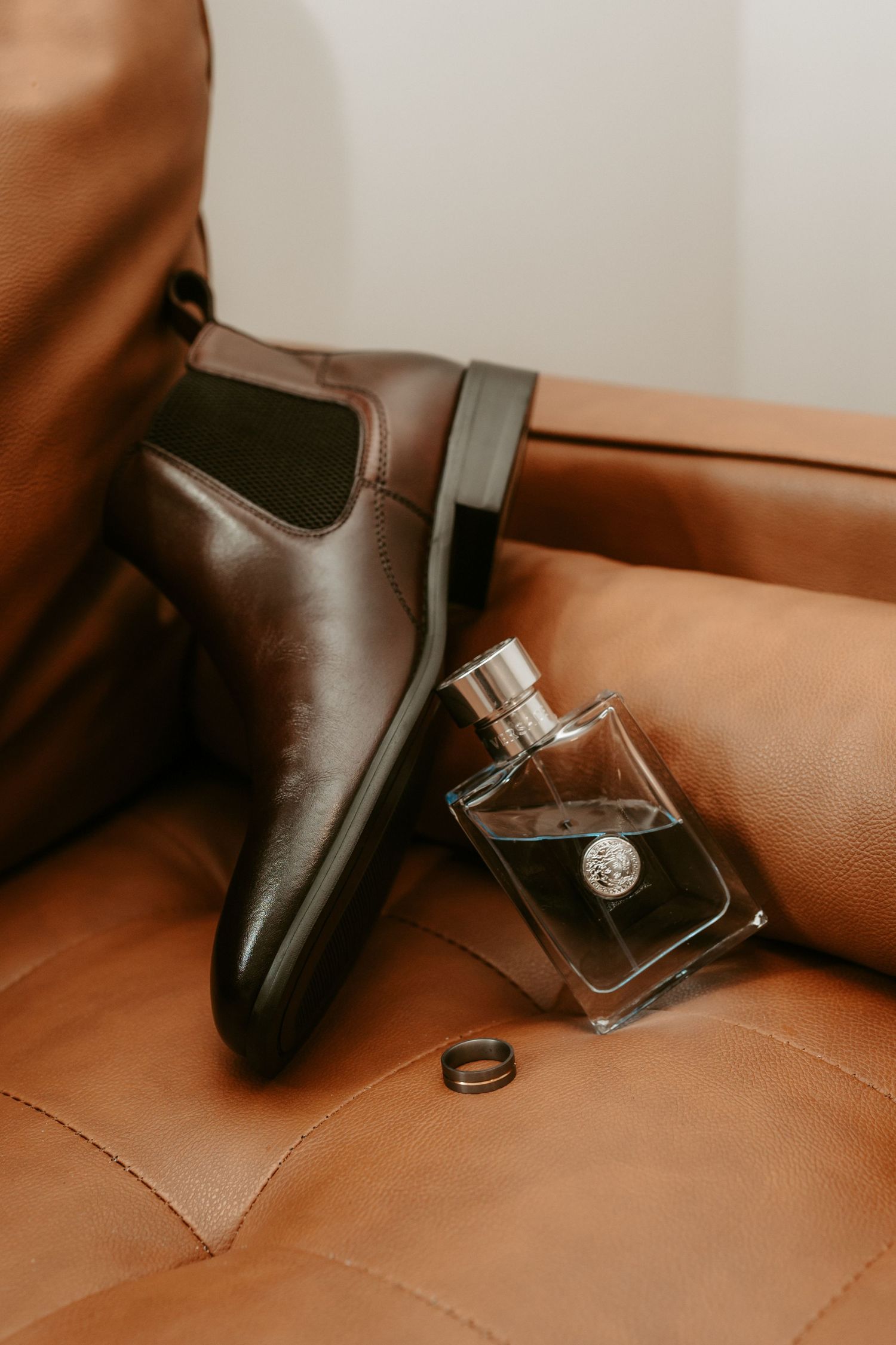Wedding details featuring rings, perfume bottle, and accessories on brown leather surface.