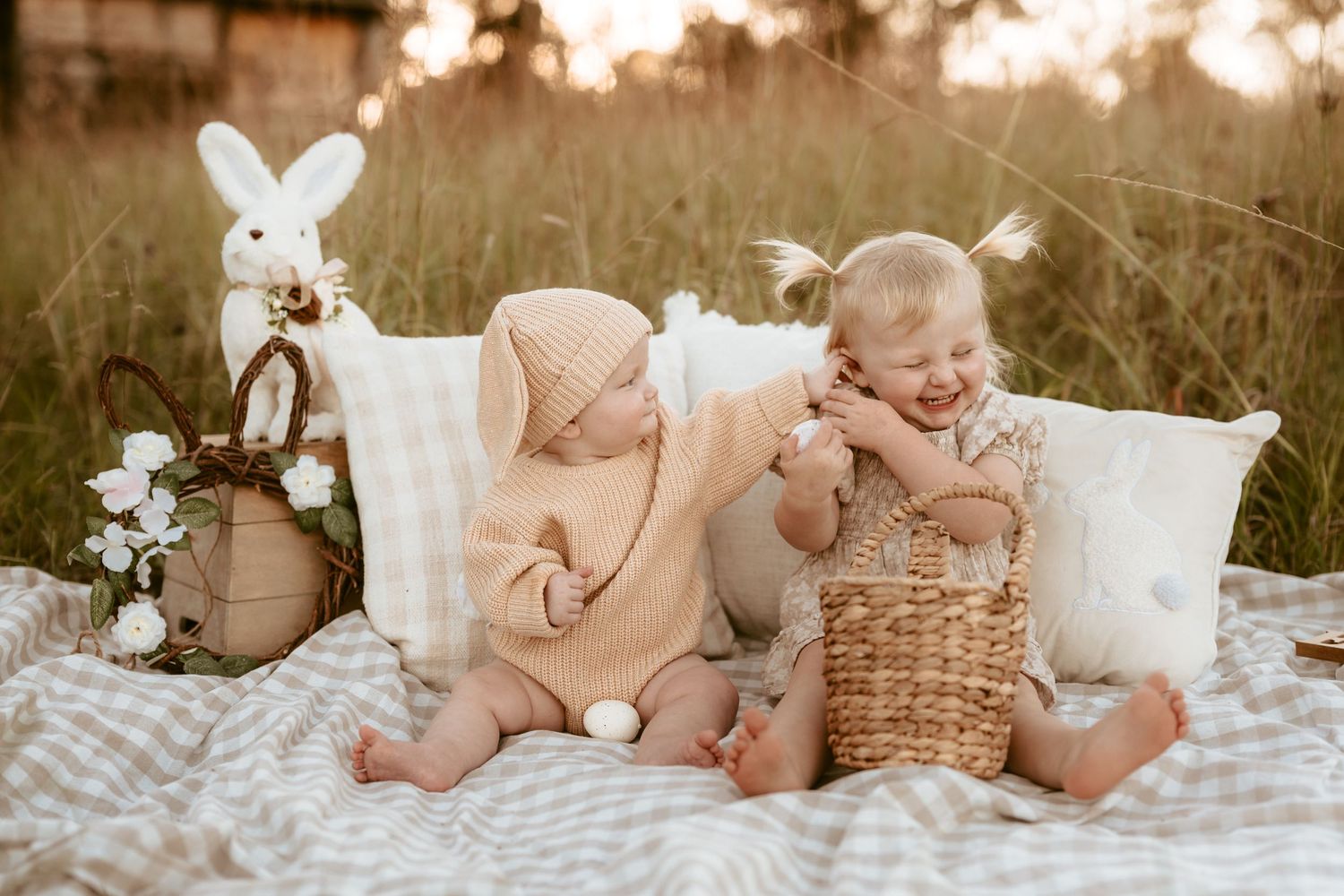 Baby photoshoot on white blanket with rustic props and bunny decorations.