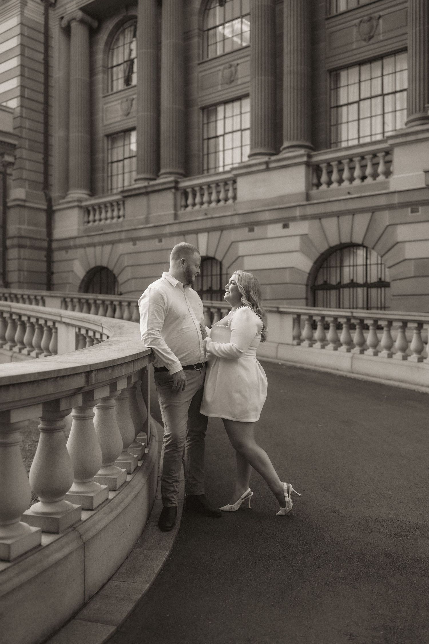 A series of black and white photos showing a couple in formal attire on an elegant balcony with stone railings.