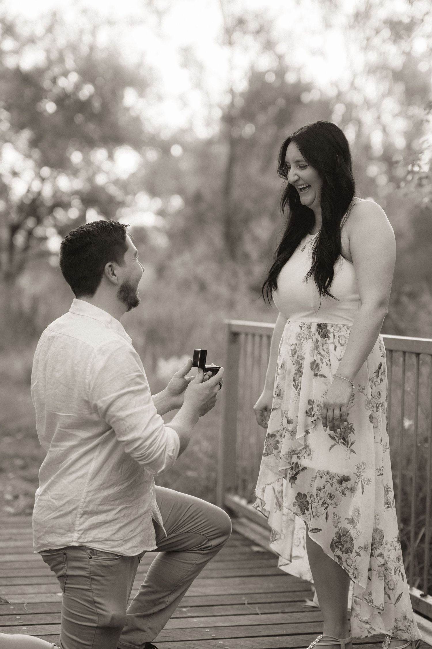 A surprise proposal moment unfolding on a wooden deck in sepia tones.