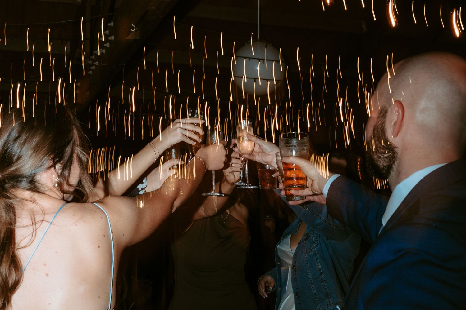 Wedding reception guests mingling in dimly lit venue with warm ambient lighting.