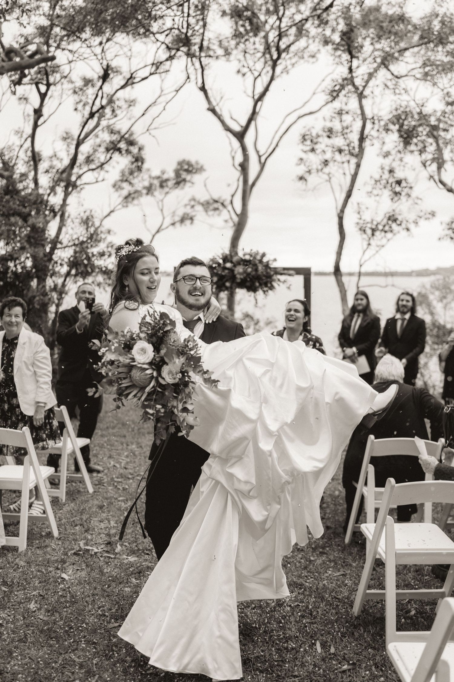 Wedding party exits ceremony through rows of white chairs on grassy lawn.