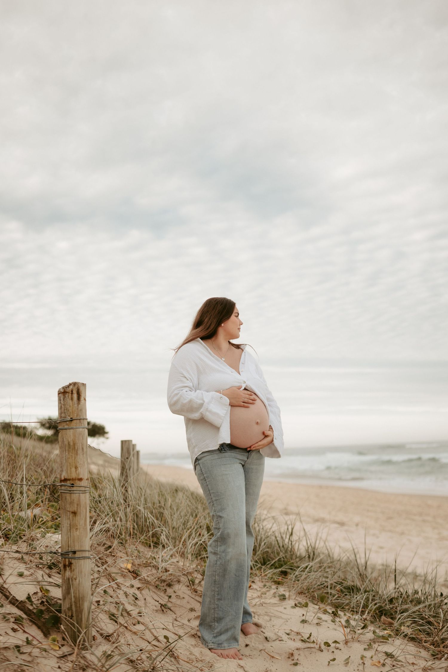 Maternity photos captured against coastal scenery with wooden fence posts.