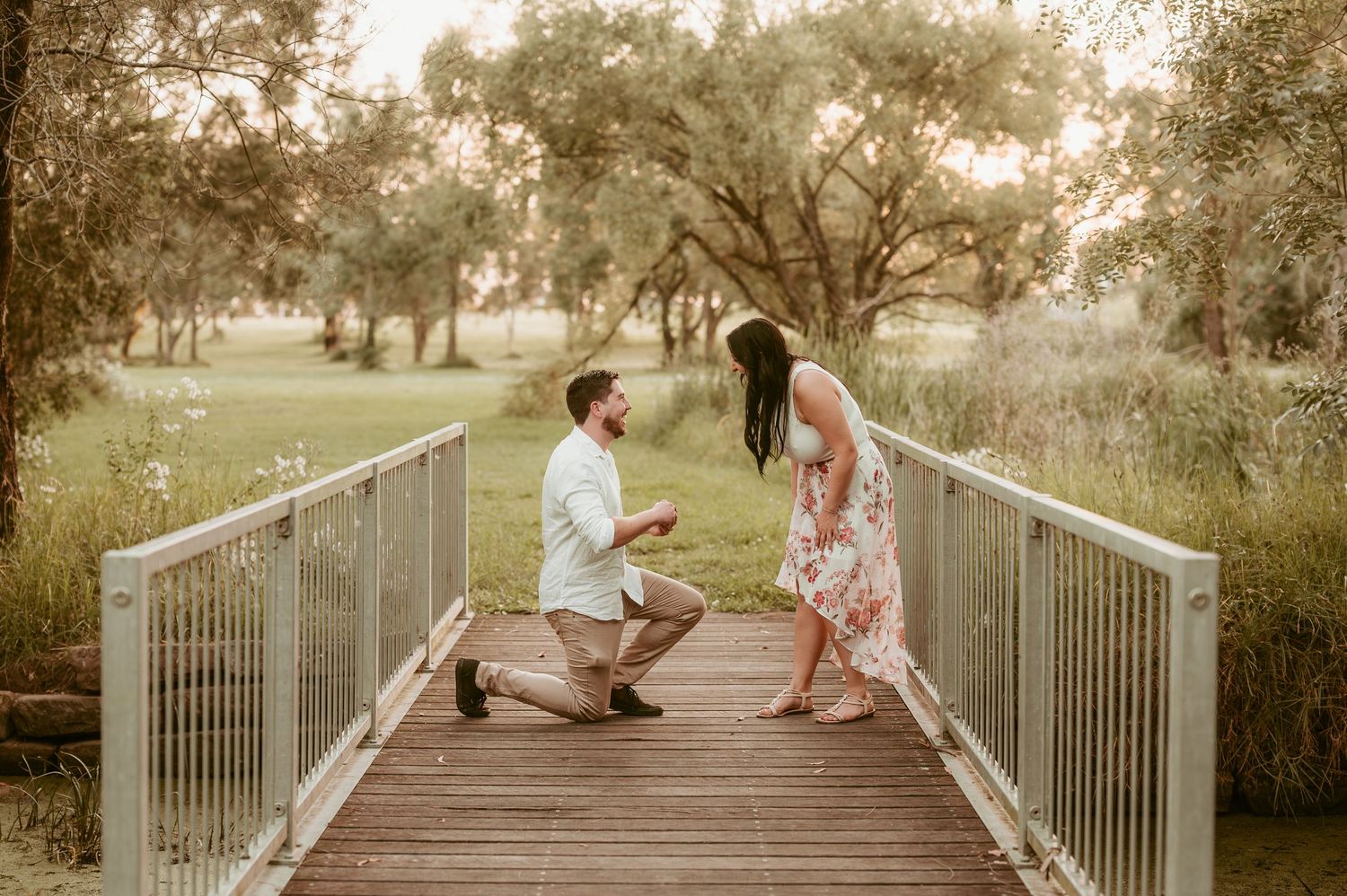 A romantic proposal sequence on a wooden bridge surrounded by trees.