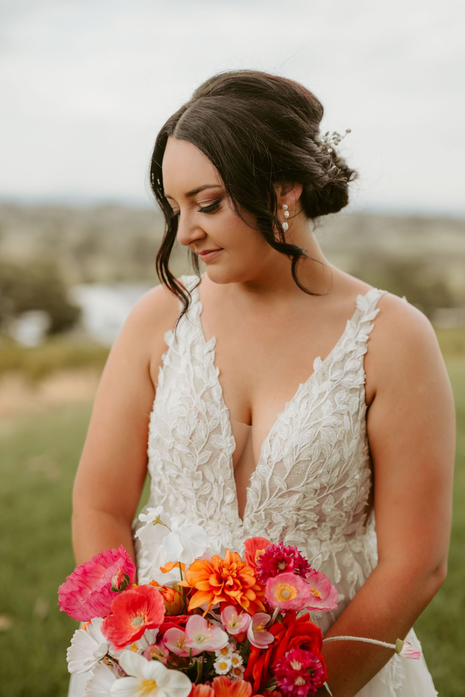 Bride in lace dress holding vibrant pink and orange floral bouquet.