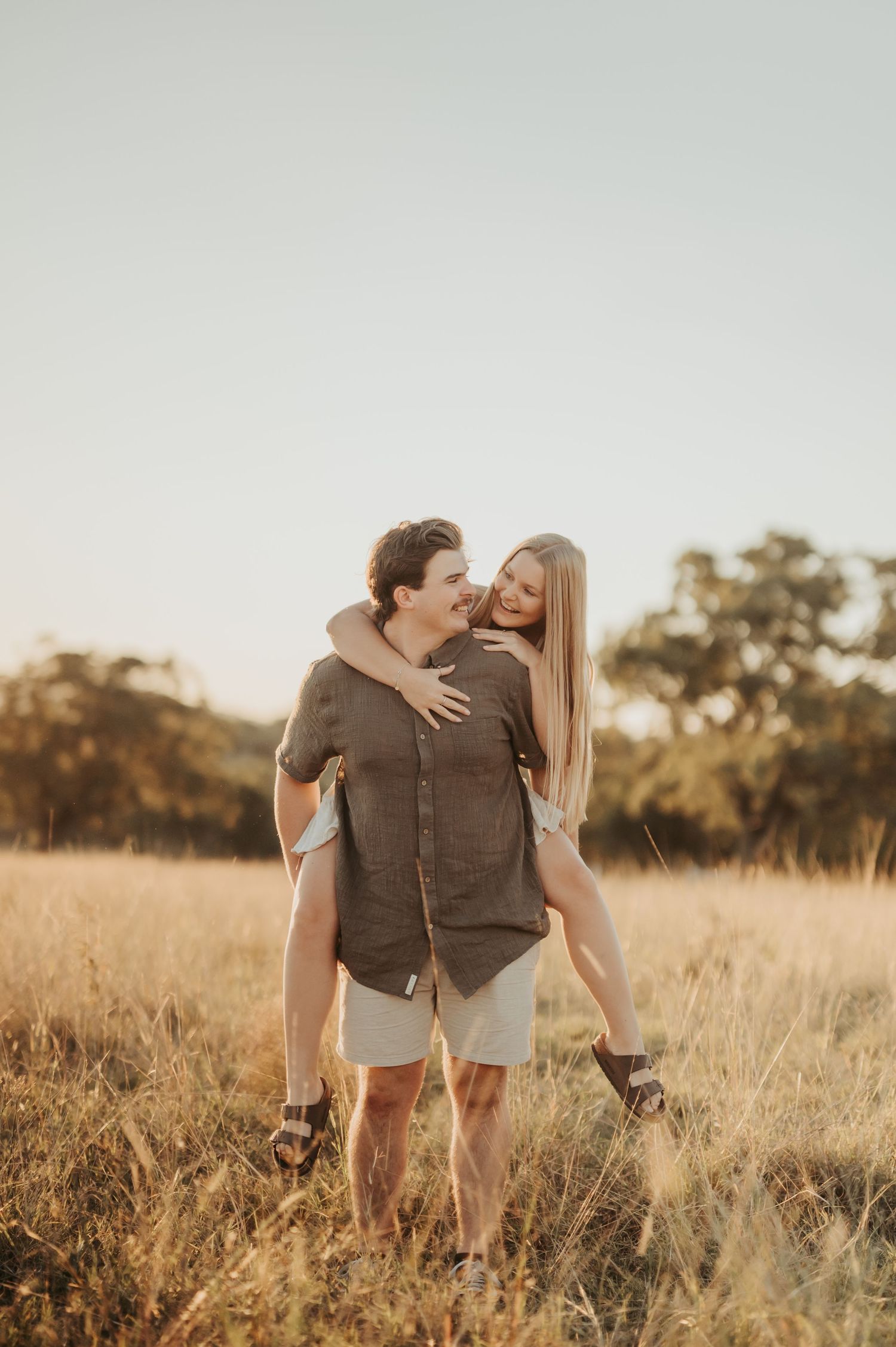 Couple embracing in a golden field during sunset with natural landscape.