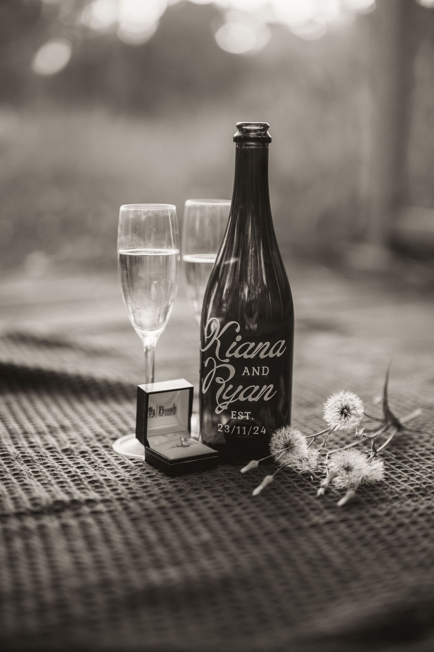 Black and white photo of wine glasses and bottles with names displayed on a textured surface.