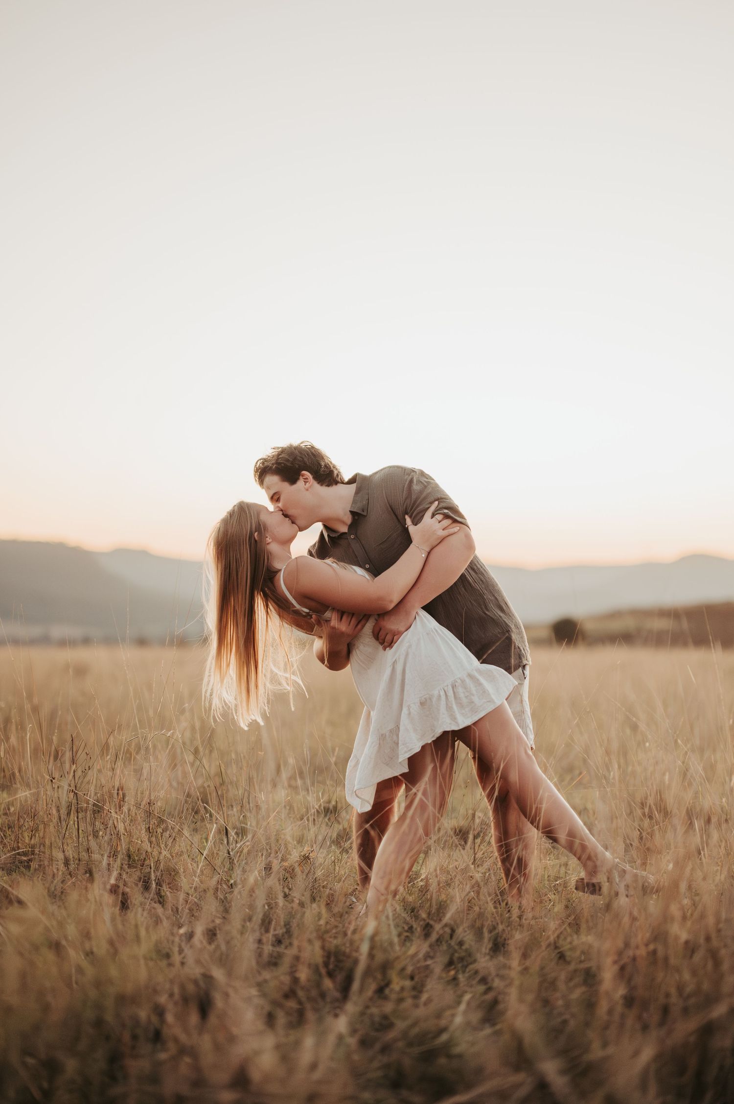 Romantic couple dancing and embracing in a sun-lit field of tall grass.