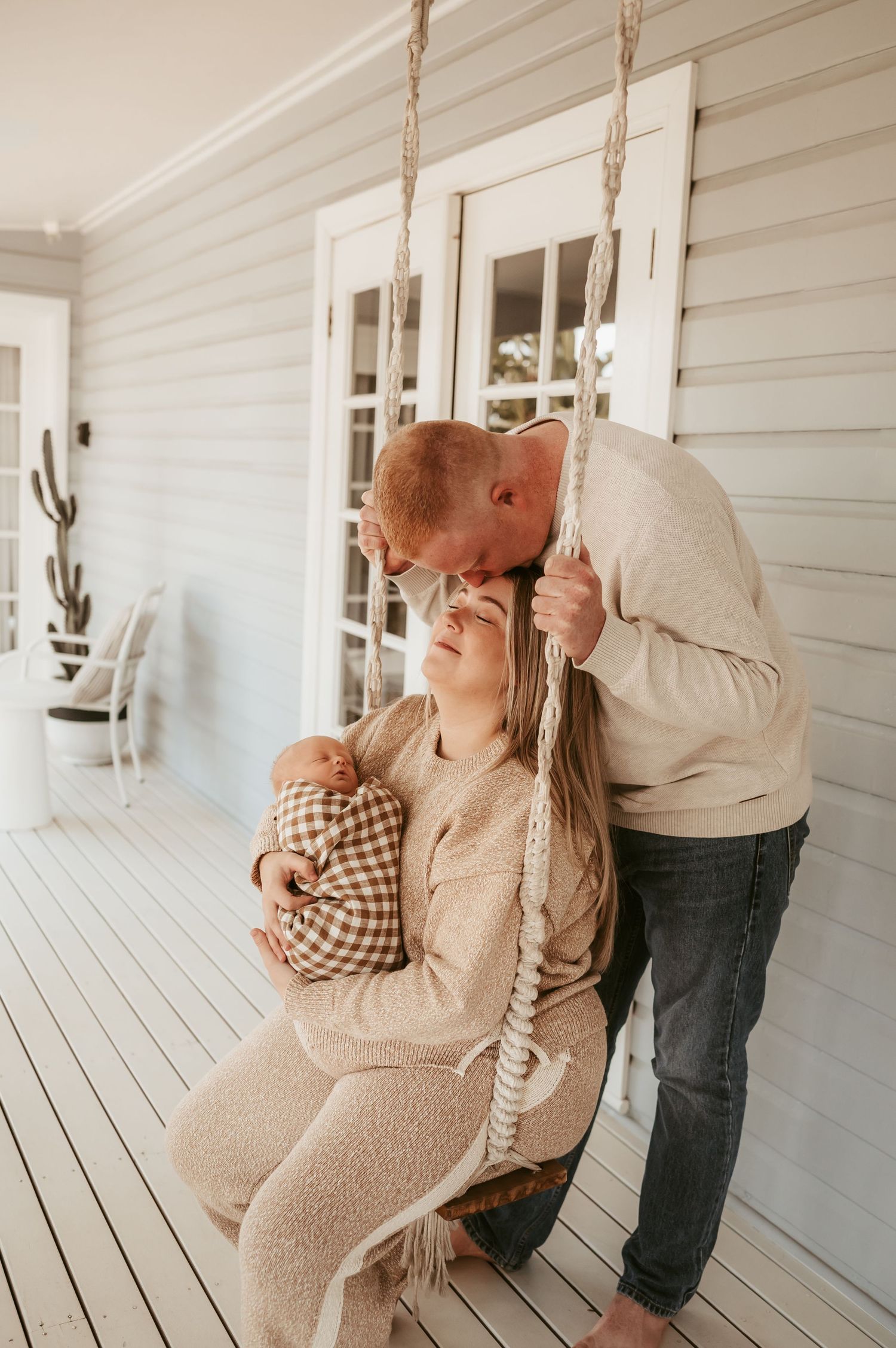 Couple sharing an intimate moment on a porch swing in front of a white farmhouse.