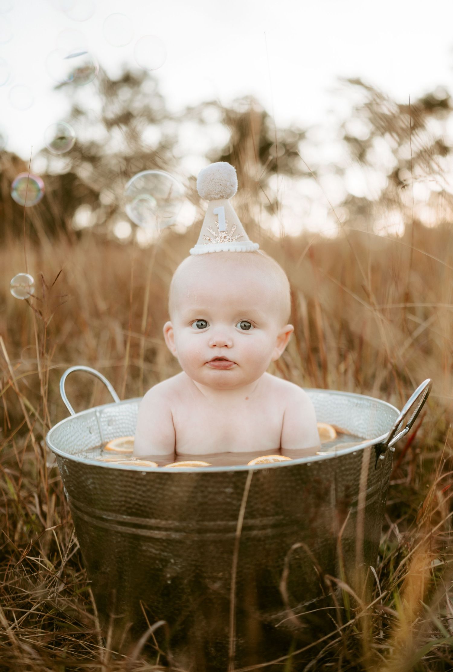 Baby sits in vintage metal tub during sunset field photoshoot.