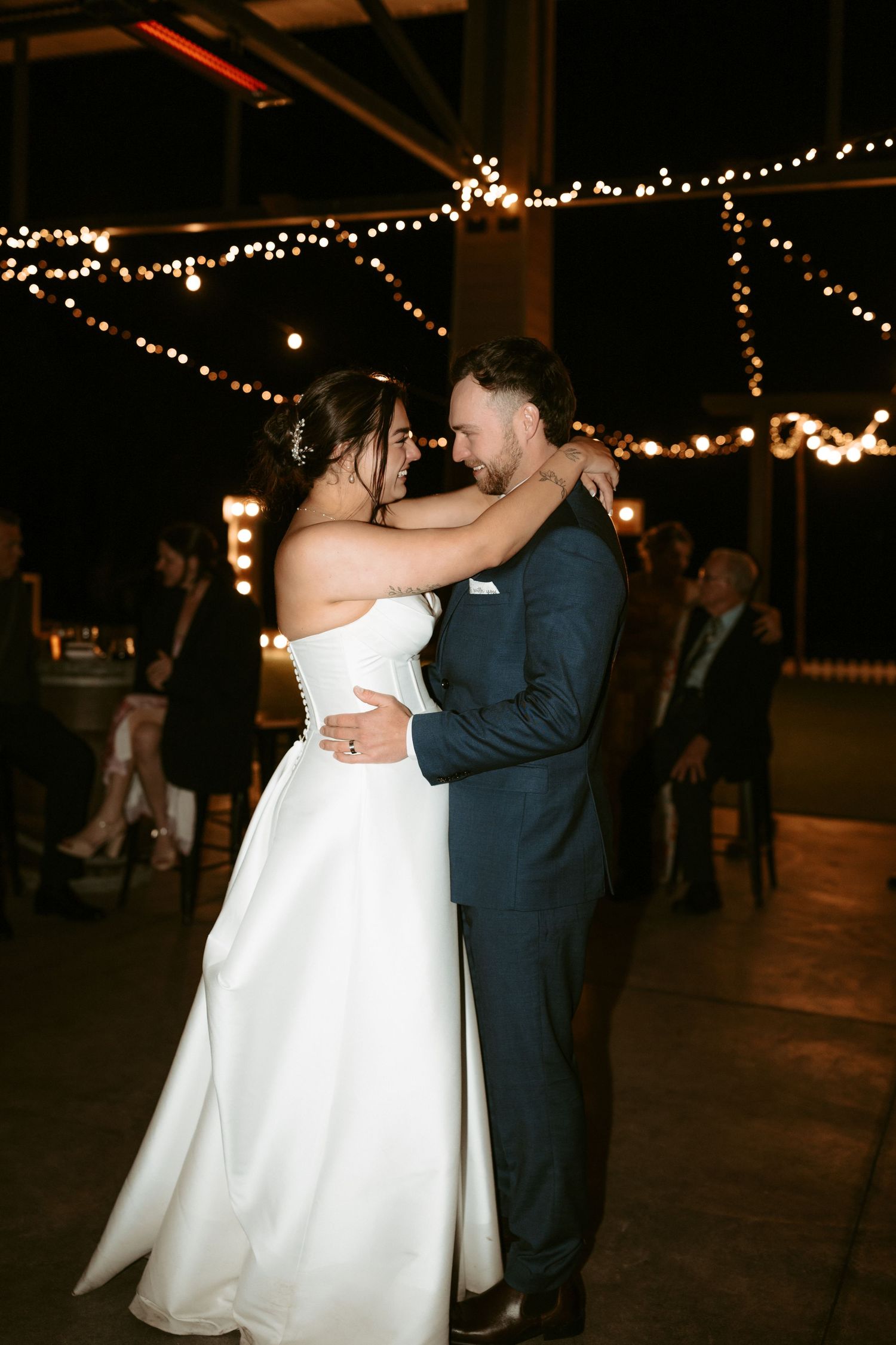 Newlyweds share their first dance under twinkling lights at an evening reception.