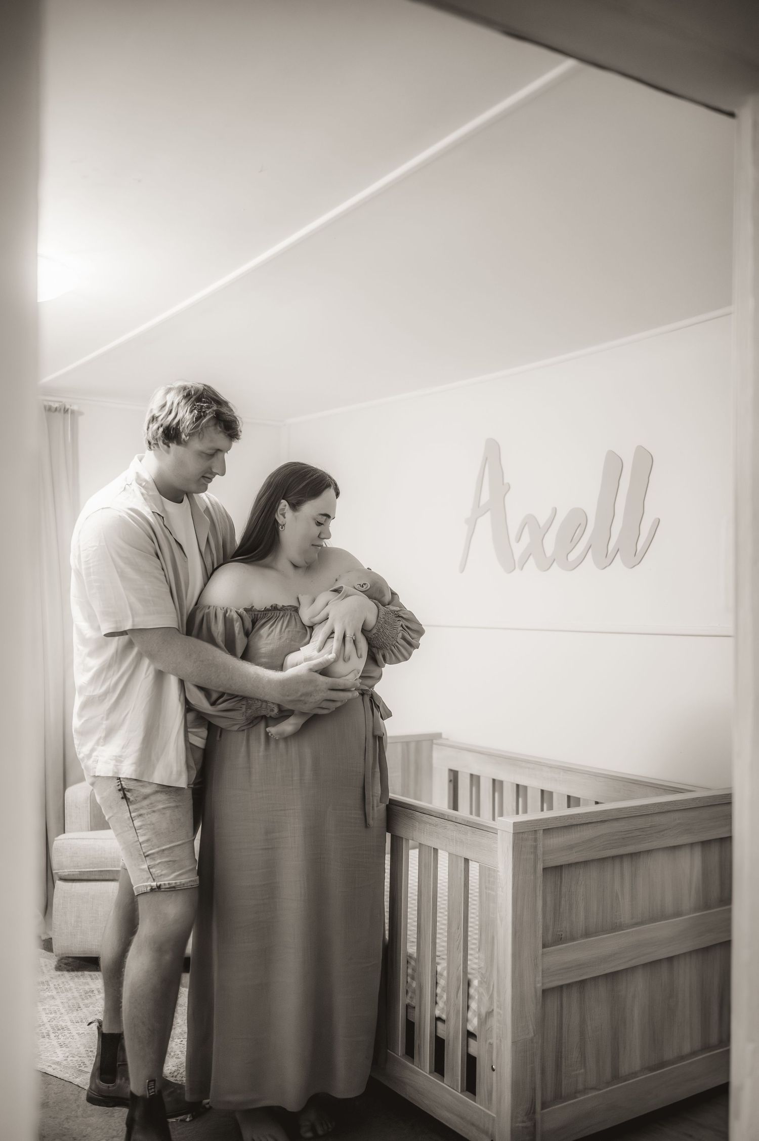 A tender moment in a nursery with a couple holding their newborn baby next to a wooden crib.