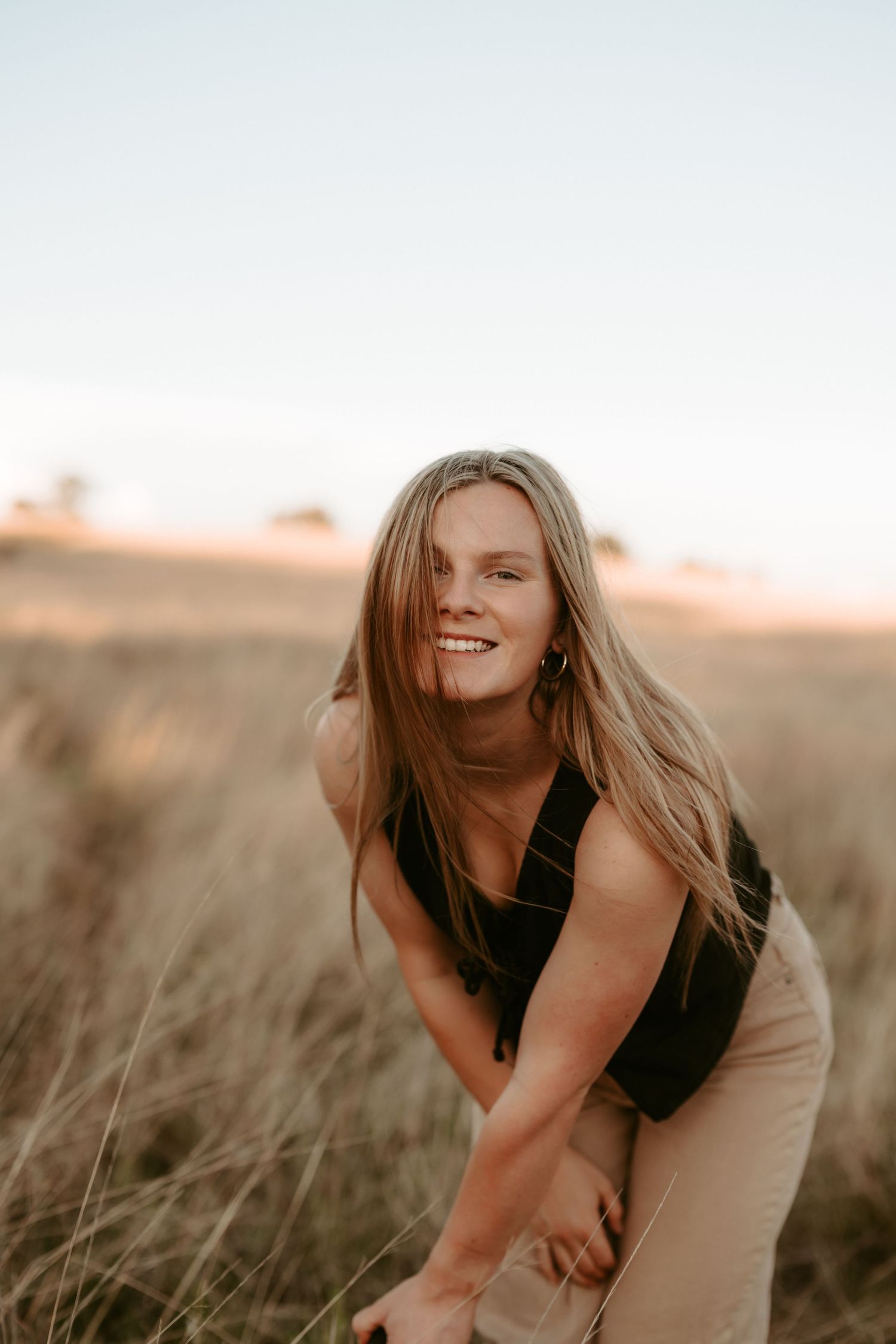 A person in casual attire laughs while standing in tall grass during golden hour.