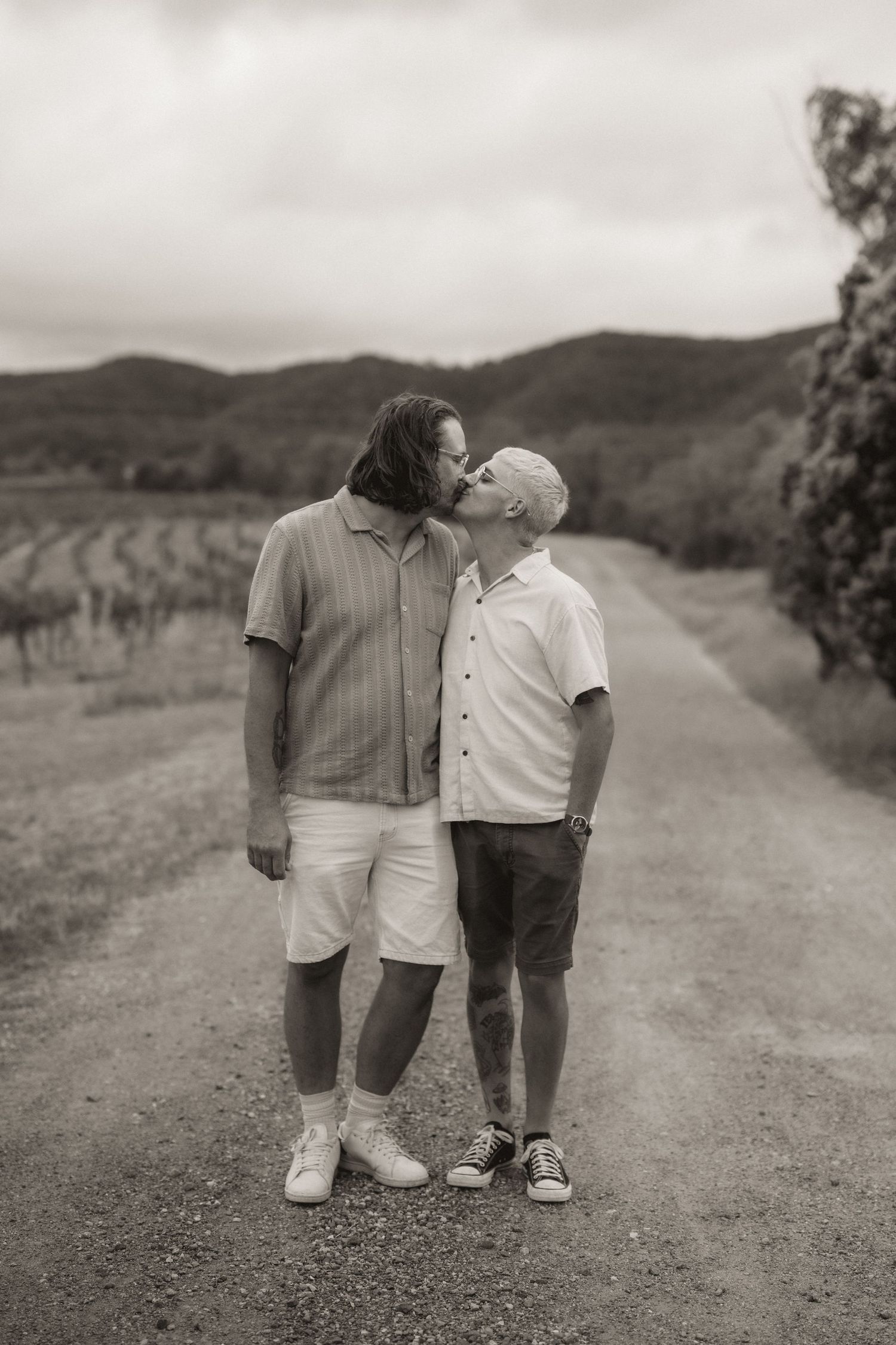 Black and white image of a couple walking on a gravel path through rolling hills.