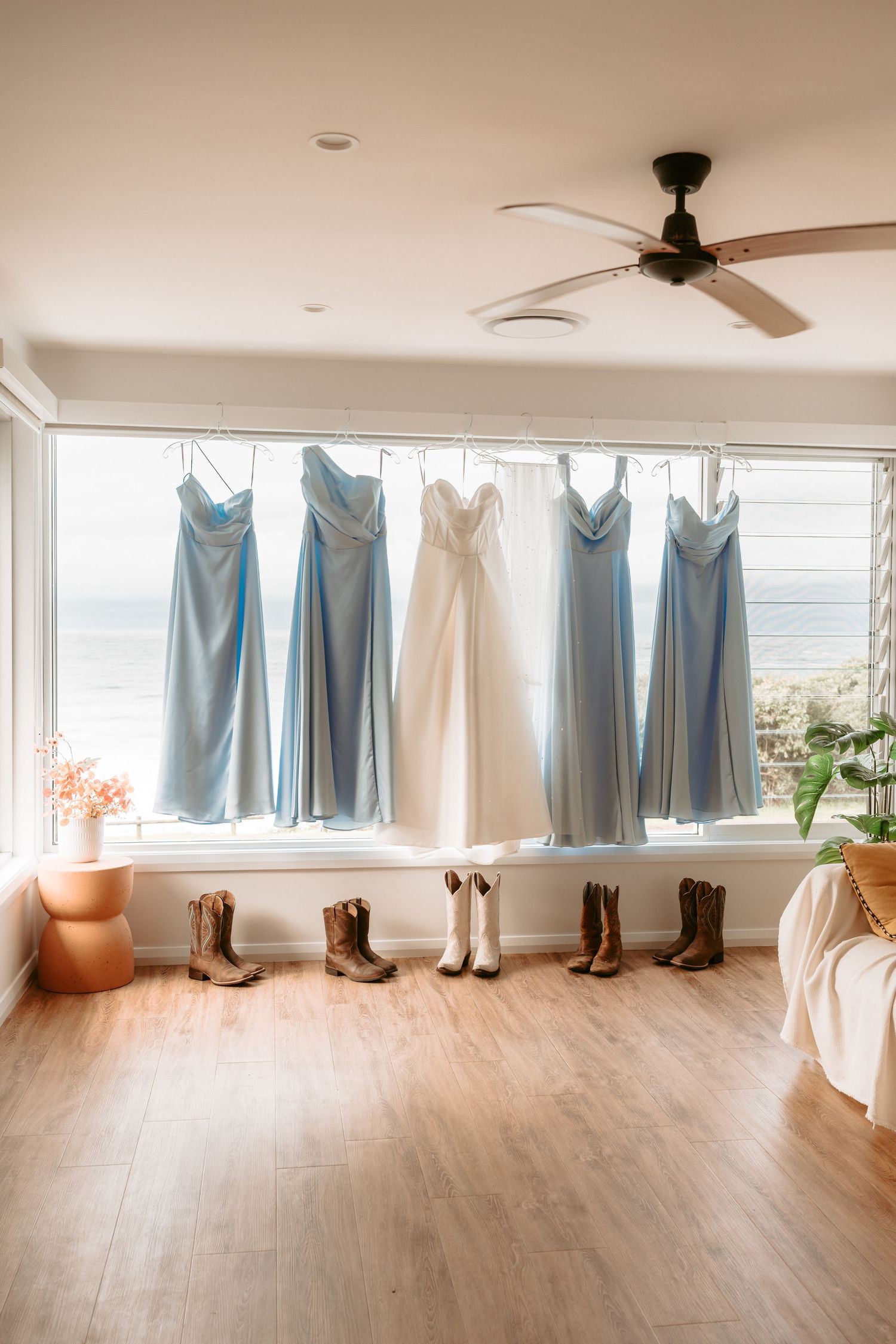 Row of light blue bridesmaid dresses and brown boots displayed against a white wall.