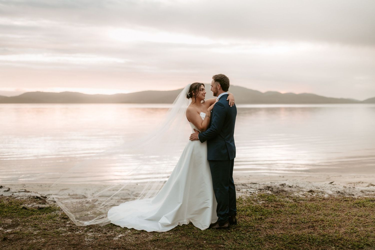 Romantic coastal wedding portraits with dramatic cloudy sky and ocean backdrop.