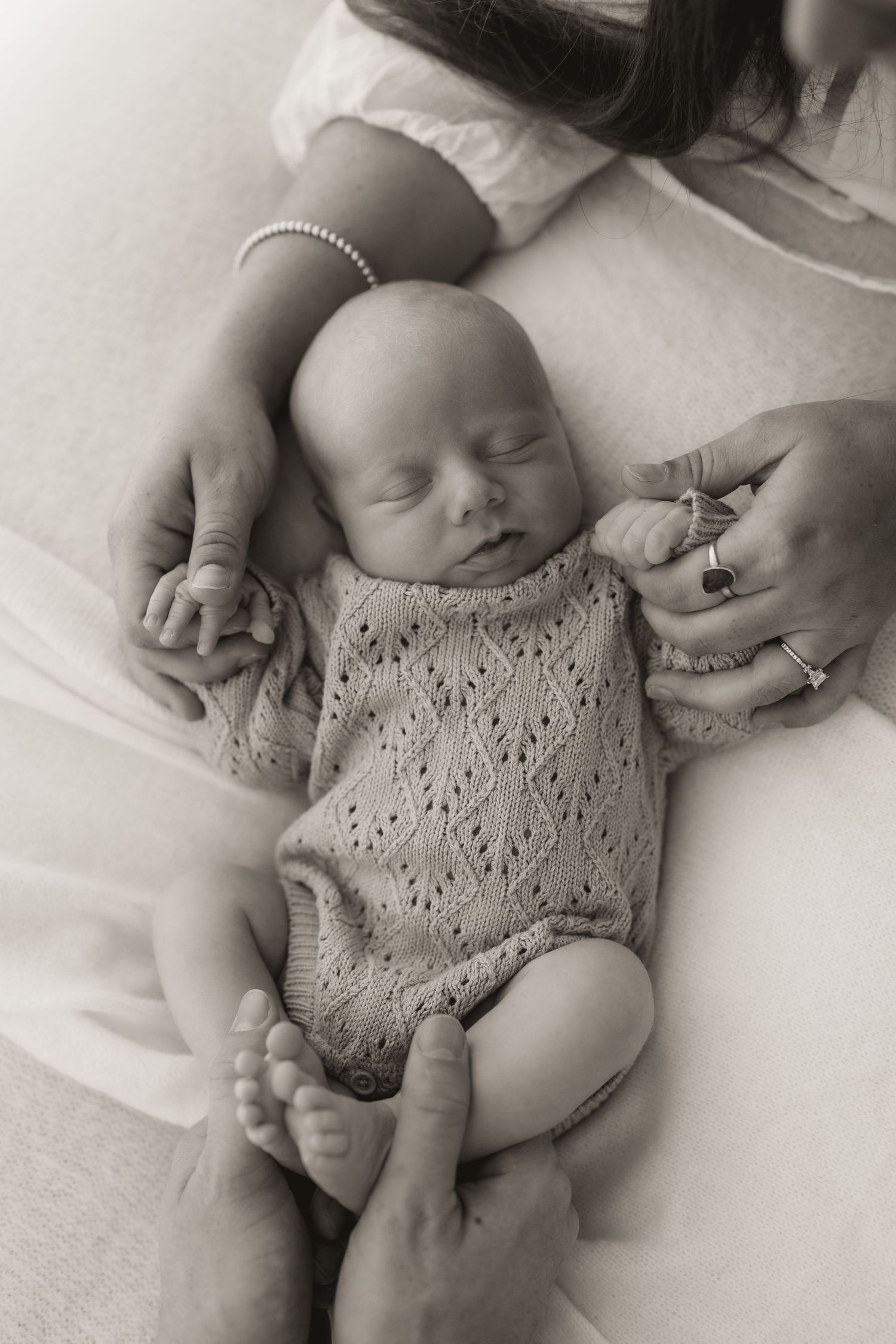 Newborn baby wearing delicate lace romper resting on white linens.