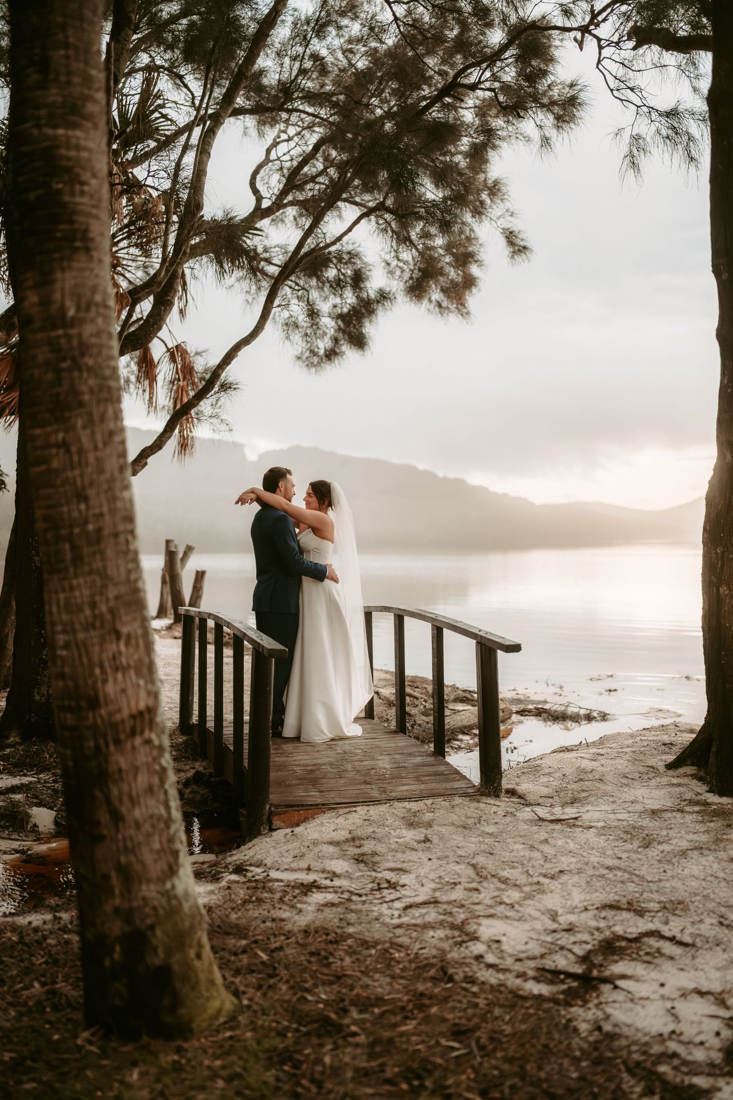 A romantic sunset wedding photo session on a wooden boardwalk surrounded by tall pine trees.