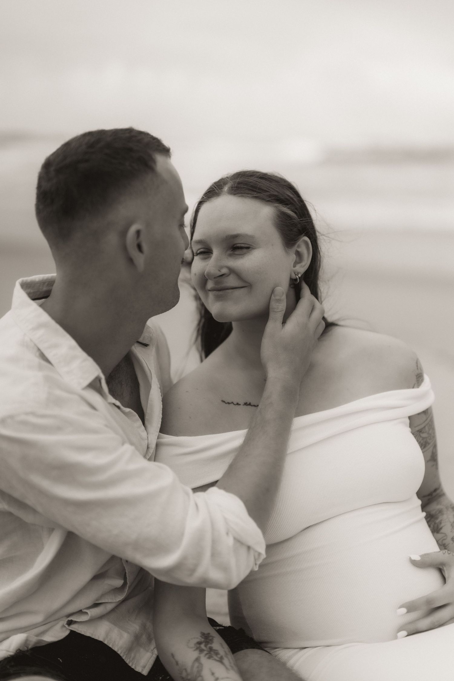 Intimate maternity photos of a couple in white clothing sharing tender moments.