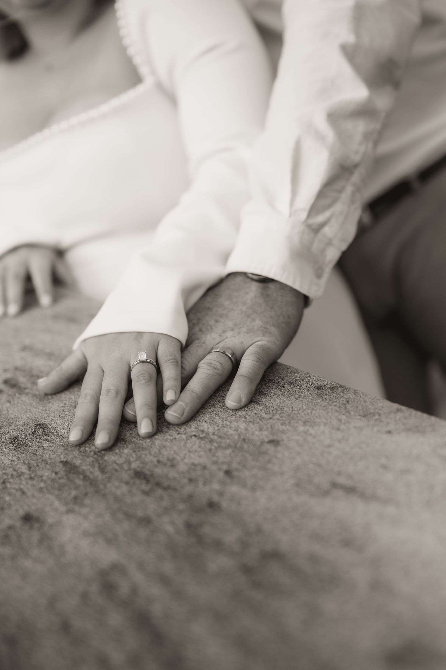 Black and white close-up of two hands resting on a textured surface, with one wearing a white sleeve.