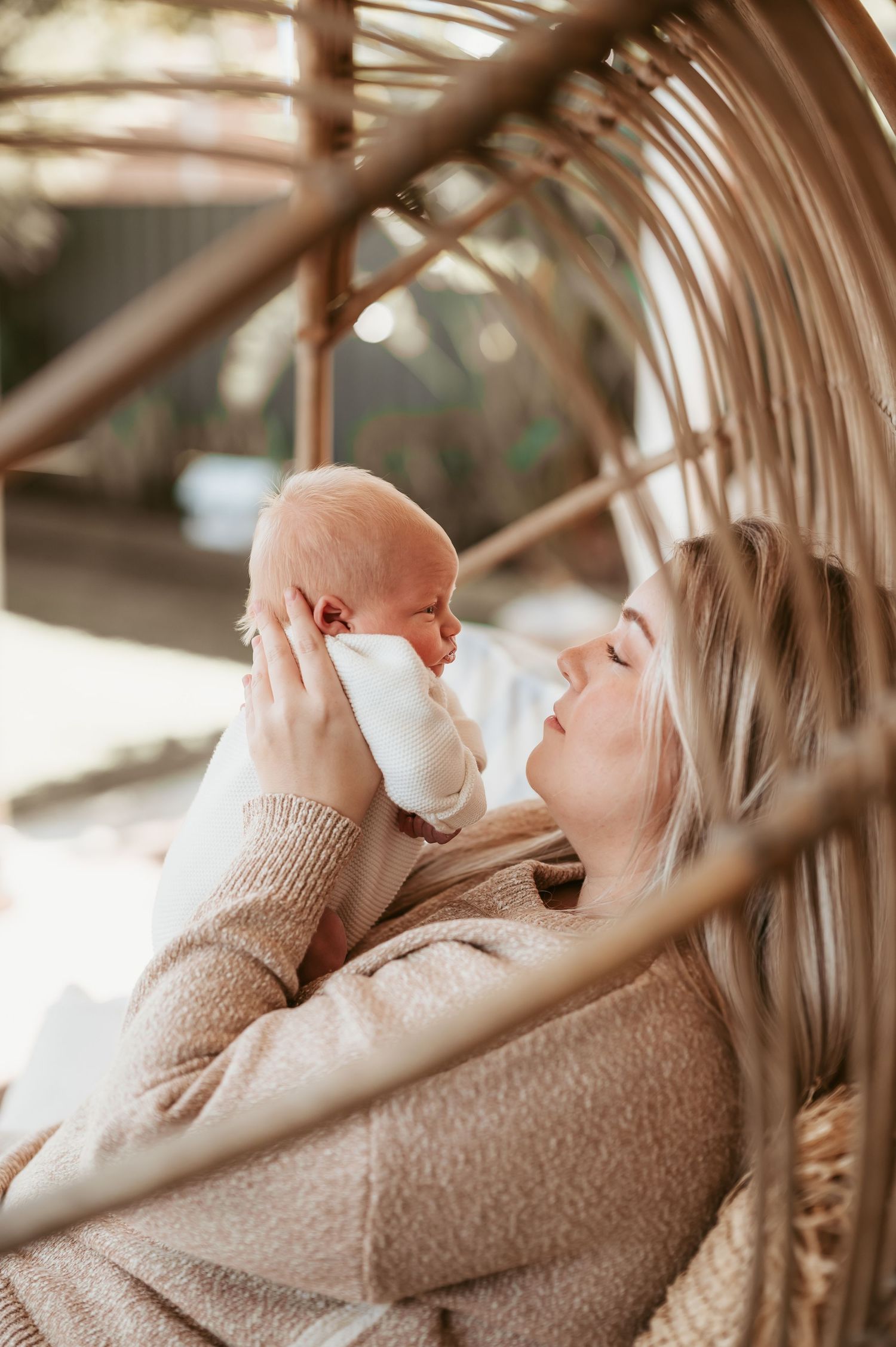Parent holding newborn baby while sitting in wicker chair with natural lighting.