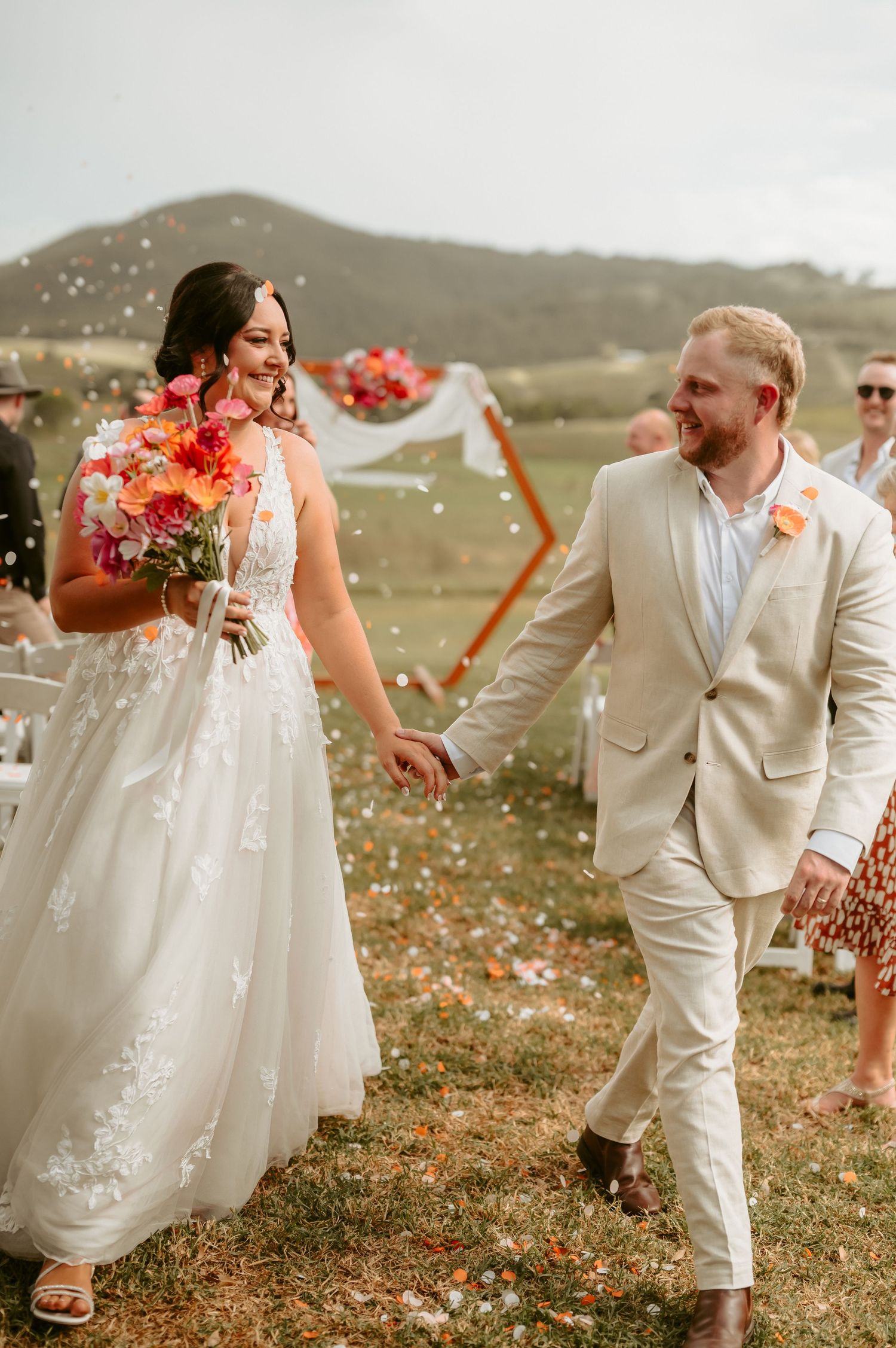 Newlyweds in white attire celebrating with confetti in an outdoor setting.