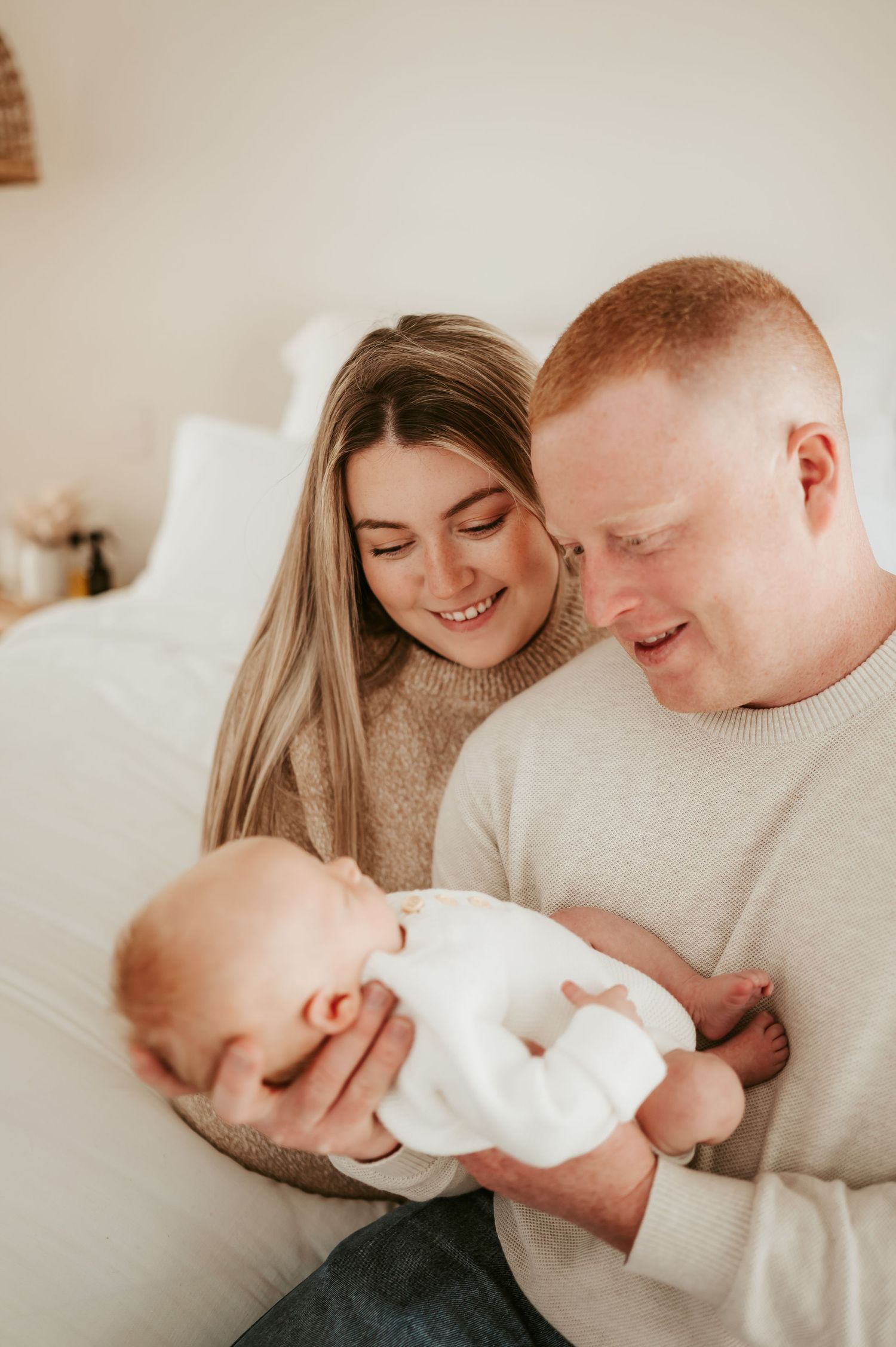 Family sharing tender moment with newborn on beige couch.