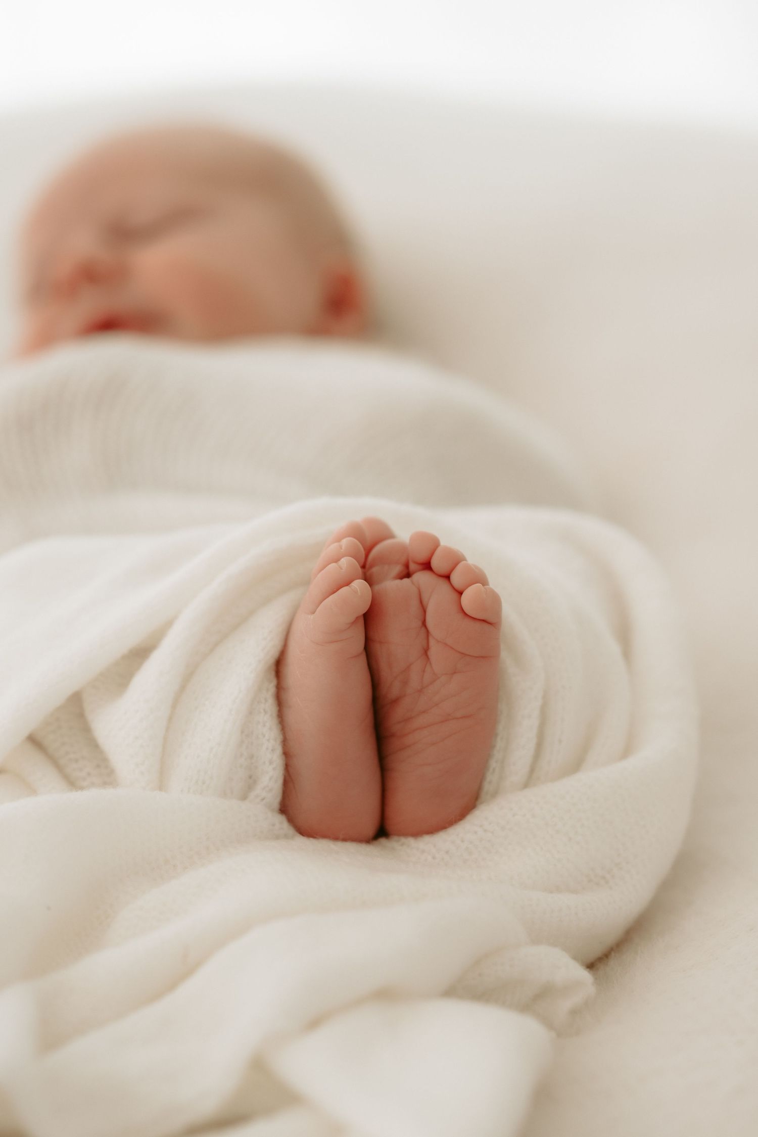 Tiny baby feet peek out from under a soft white blanket.