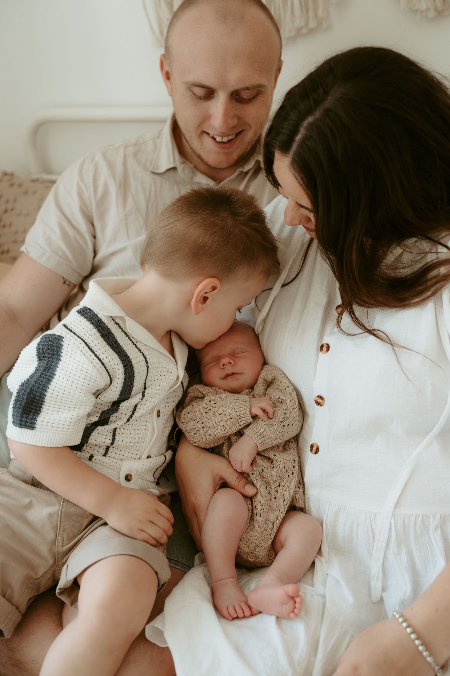 Family snuggling together on white couch with newborn baby.