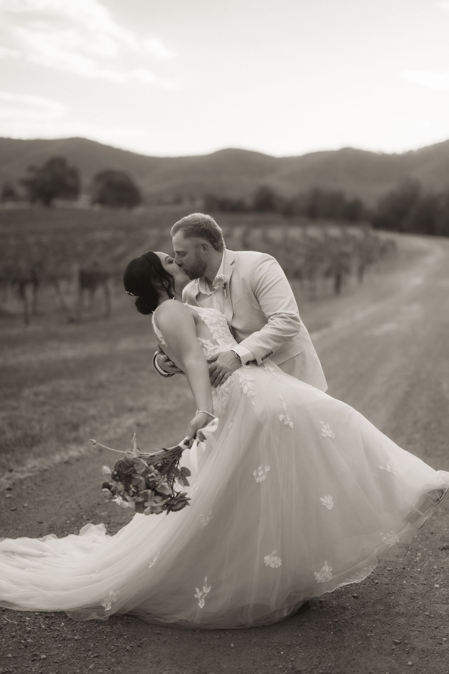 Black and white portrait of newlyweds in classic dip pose at a vineyard.