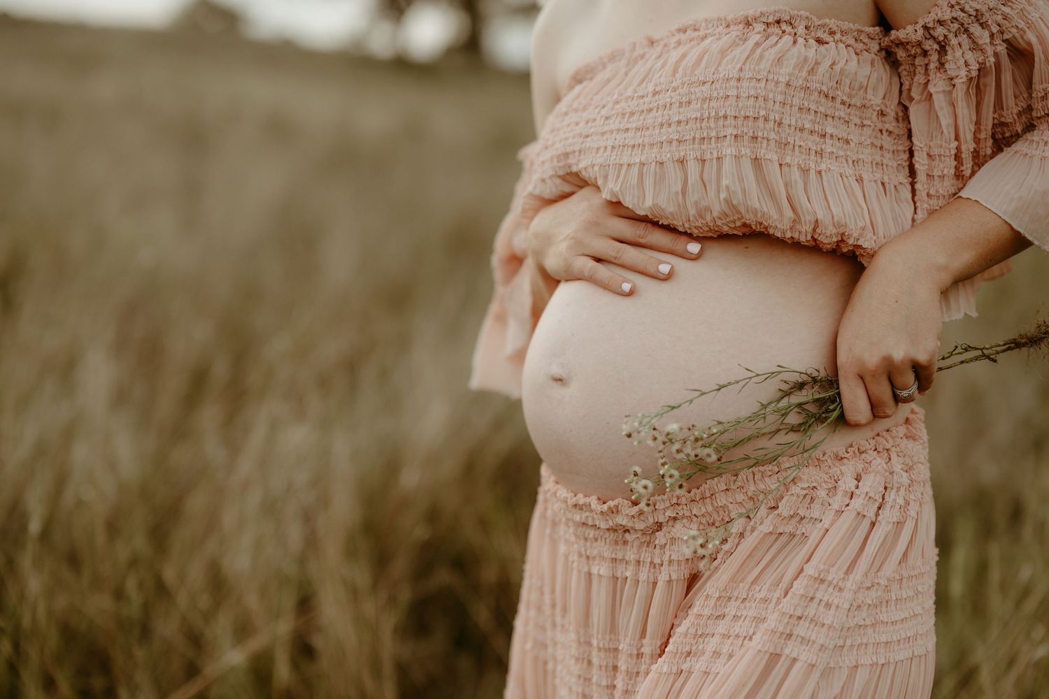 A close-up maternity photo showing hands cradling a pregnant belly in a pink gown.