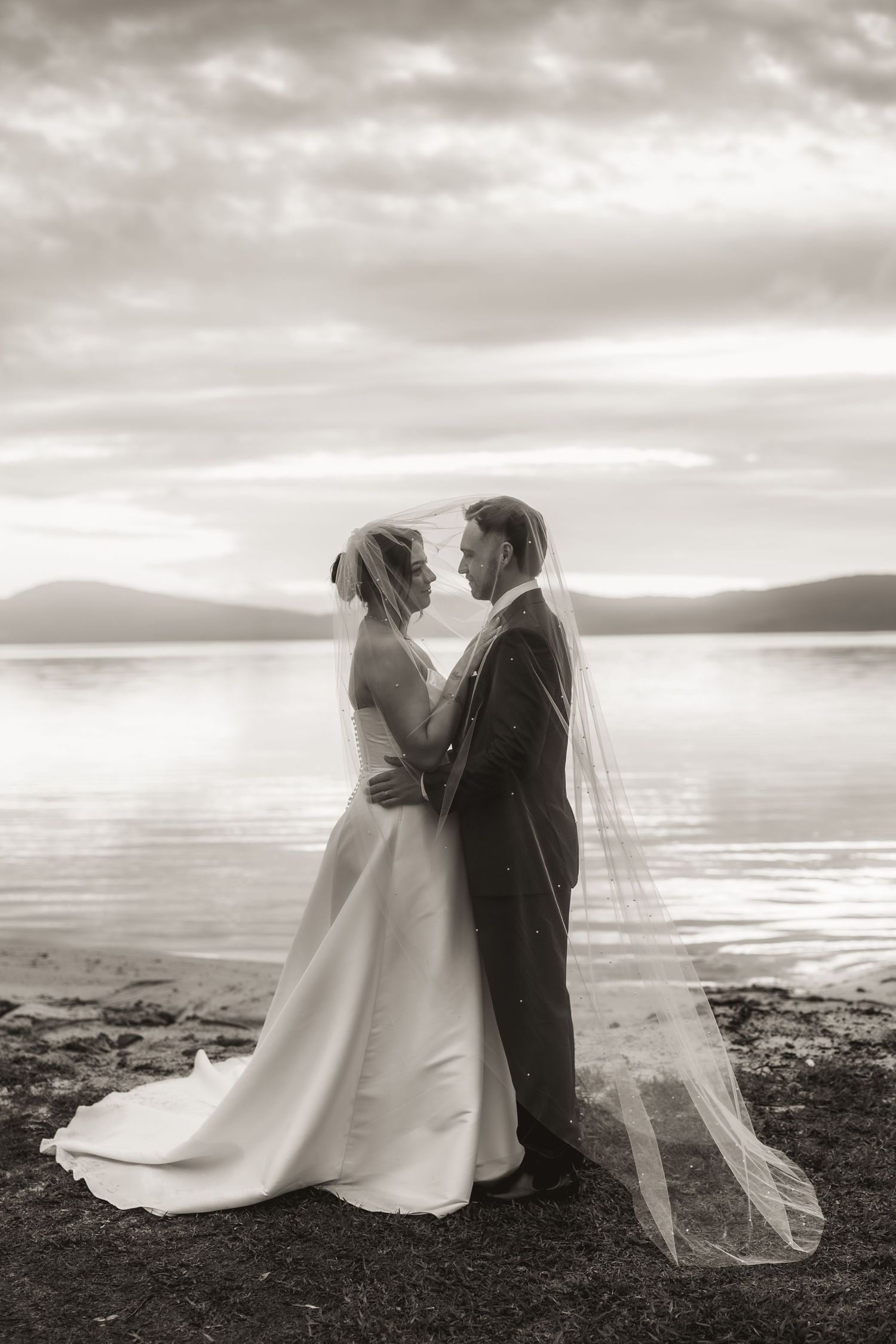 Black and white wedding portraits on a moody beach with dramatic clouds.