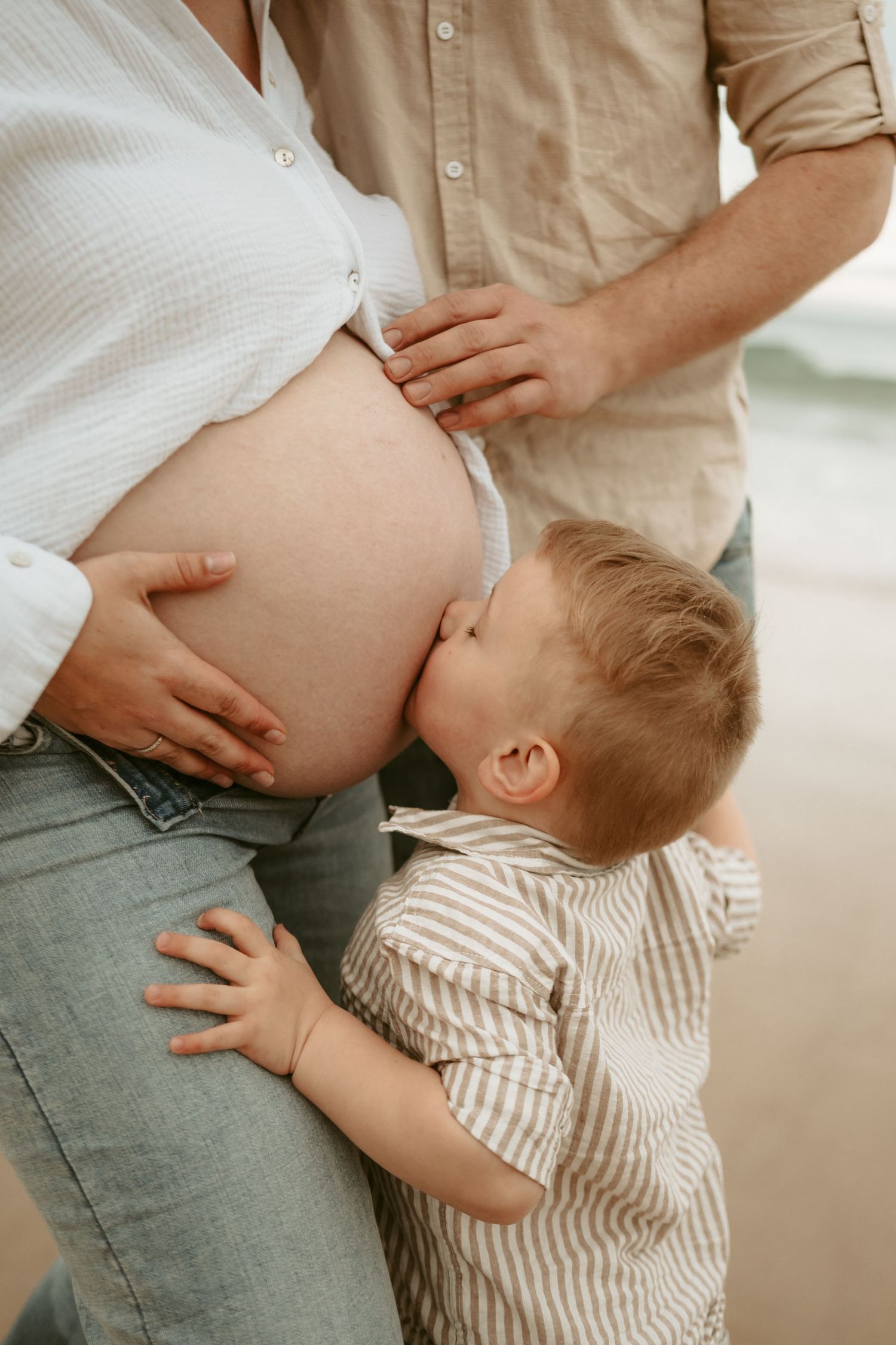 A sweet moment showing a toddler embracing an expectant mother's belly on the beach.