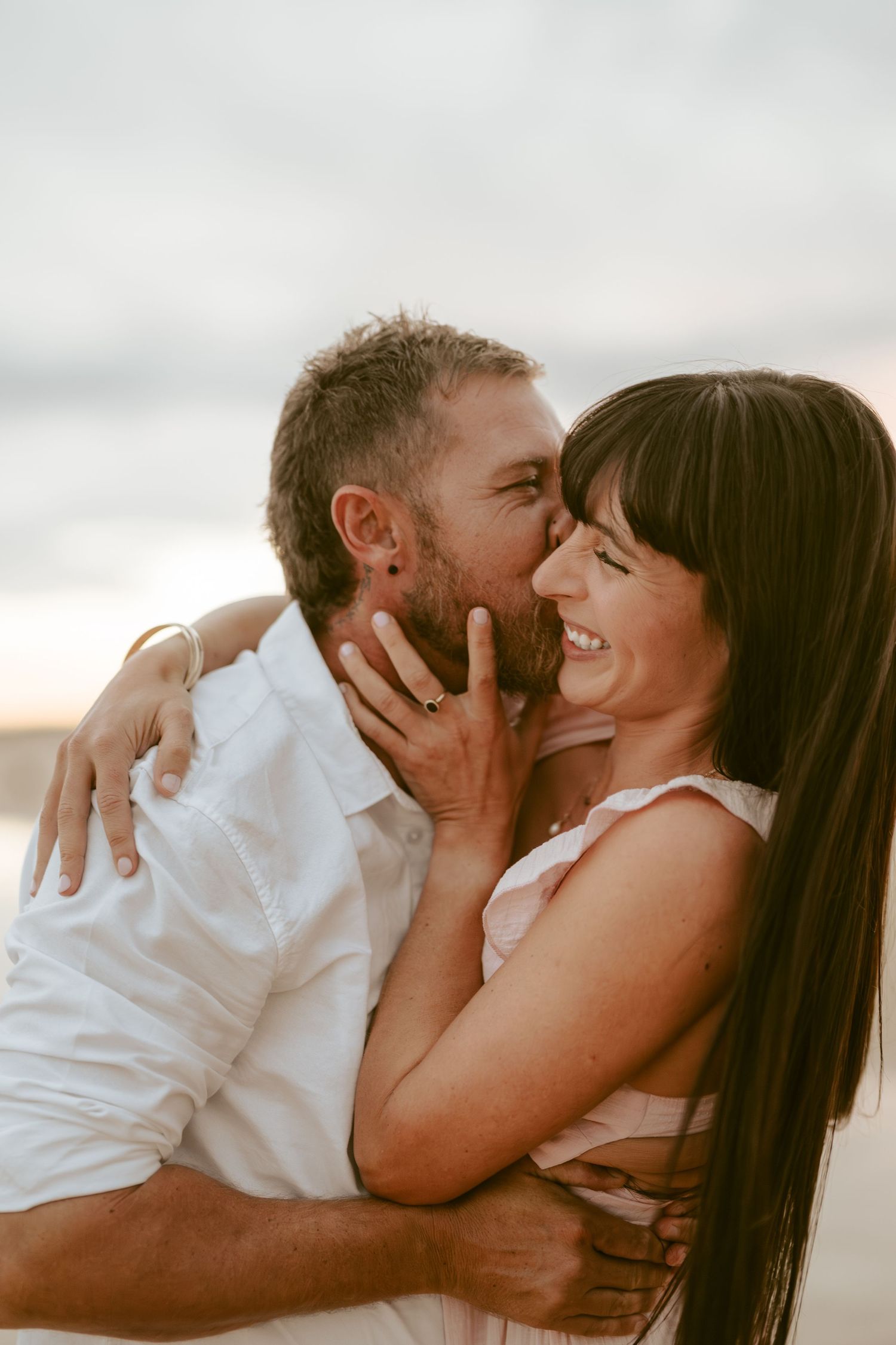 Intimate couple sharing romantic moments on a beach during golden hour.