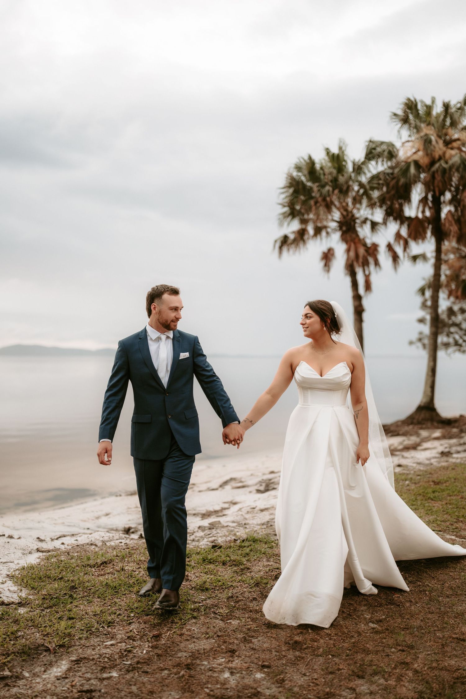 Couple walking along coastal path with palm trees in background.