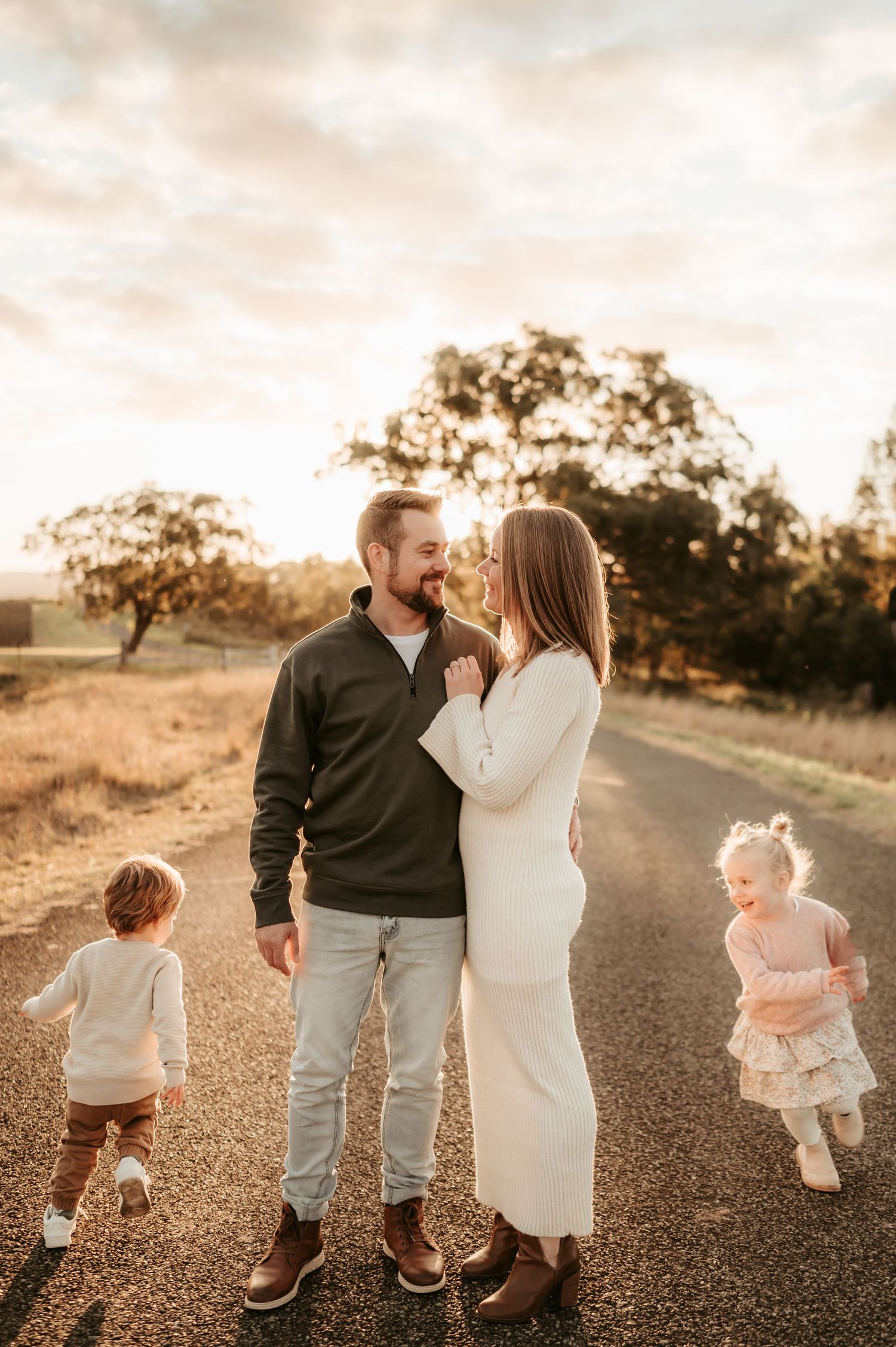 A family walks together on a dirt path at sunset with children playing nearby.