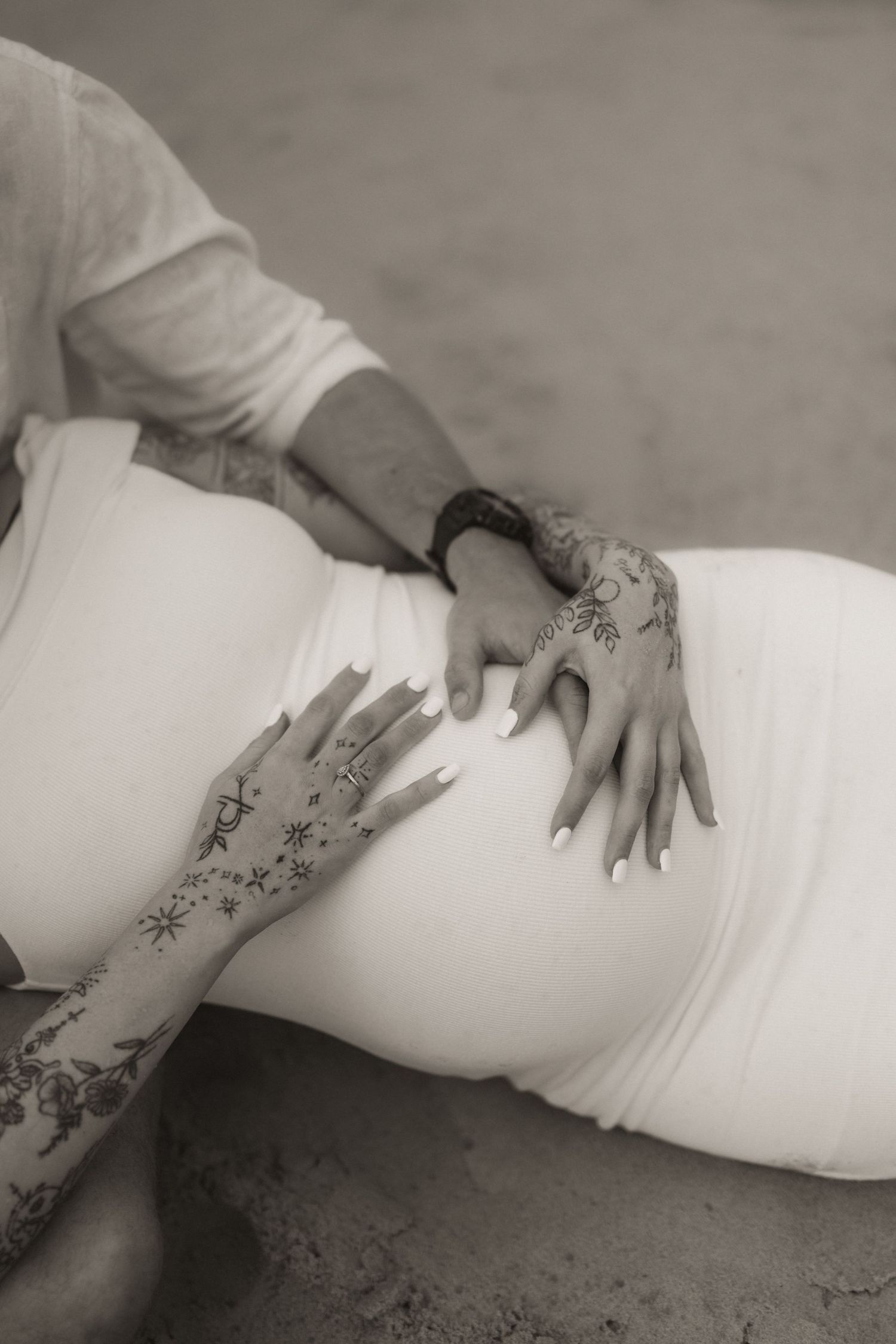 Close-up shots highlighting tattooed arms cradling a pregnant belly in a white dress.