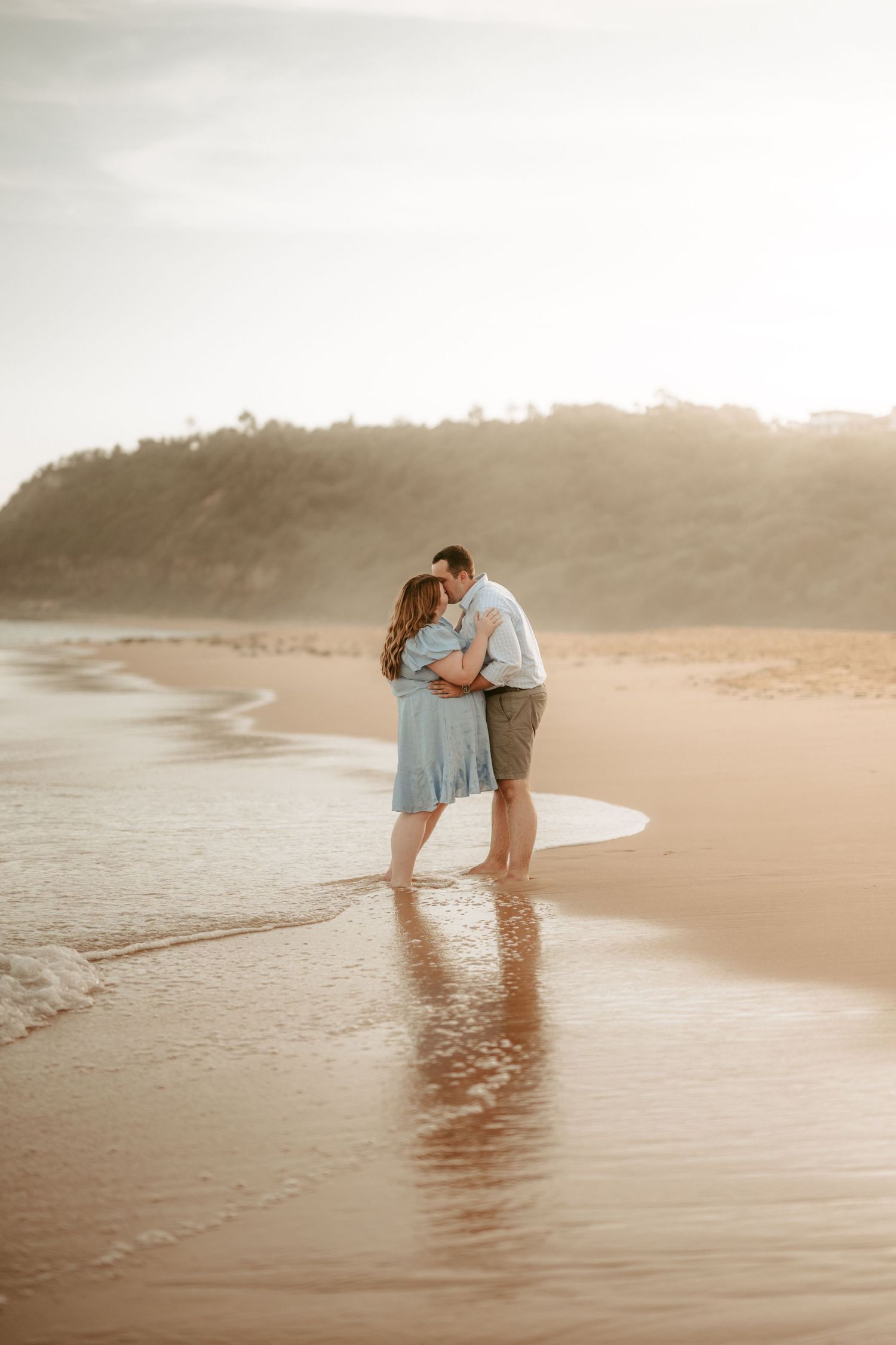 Couple in light clothing sharing romantic moments at sunset on a beach.