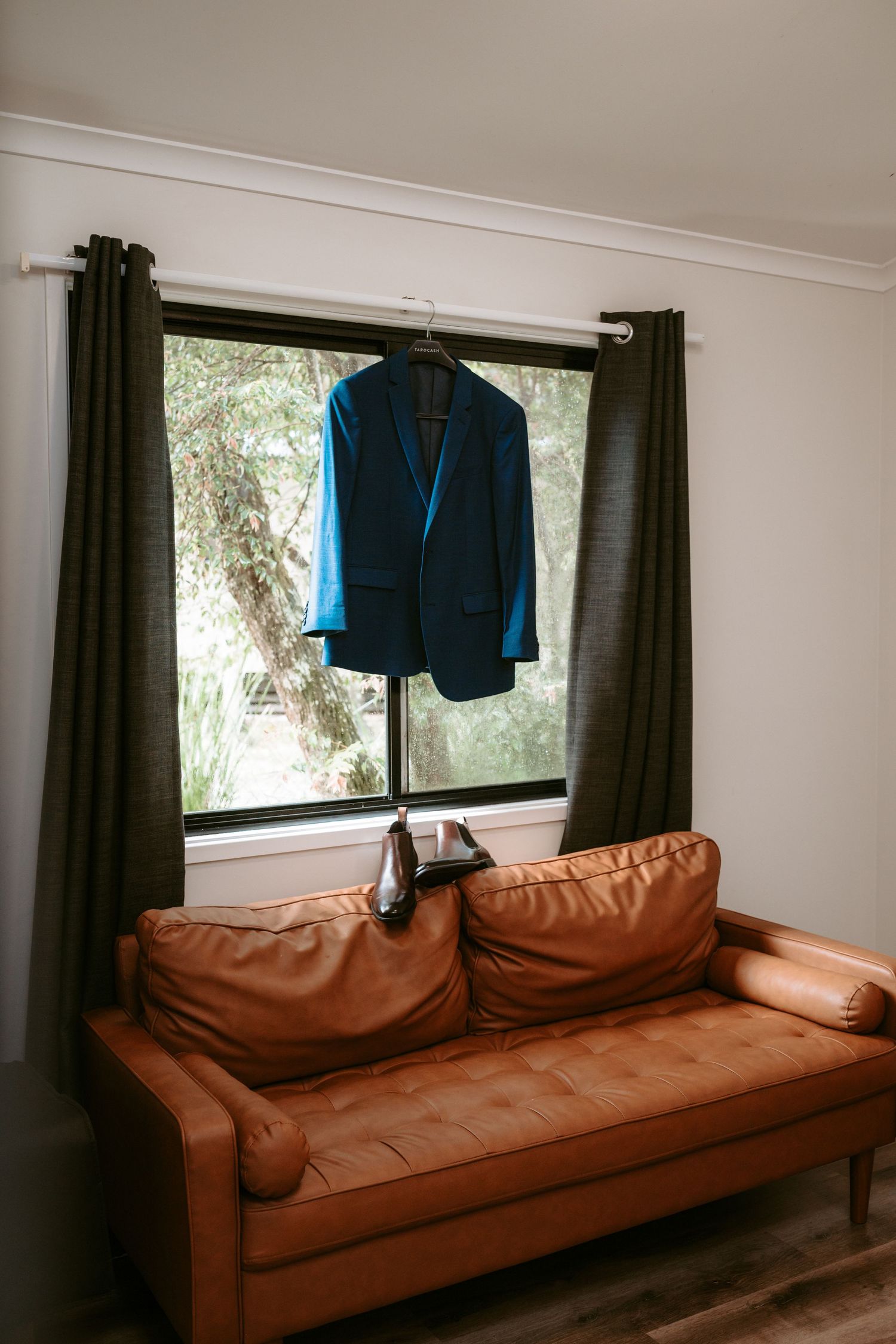 Brown leather couch with blue suit jacket hanging by window in preparation room.