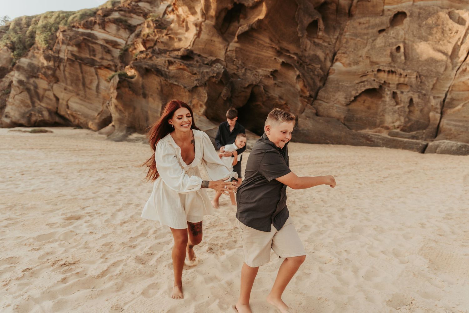 A couple runs joyfully along a beach with rocky cliffs in the background.