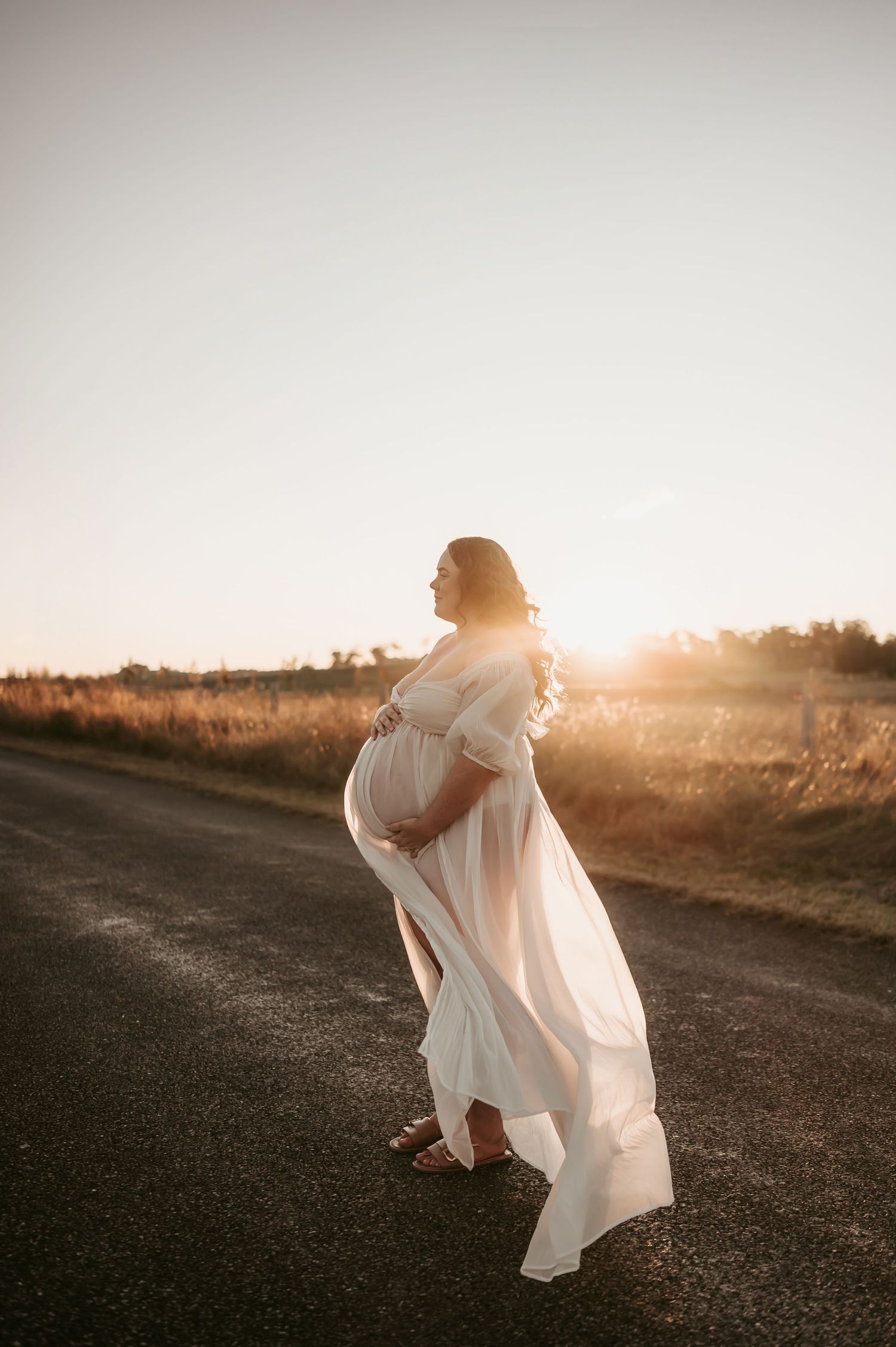 A flowing white dress catches the golden sunset light on a rural dirt path.