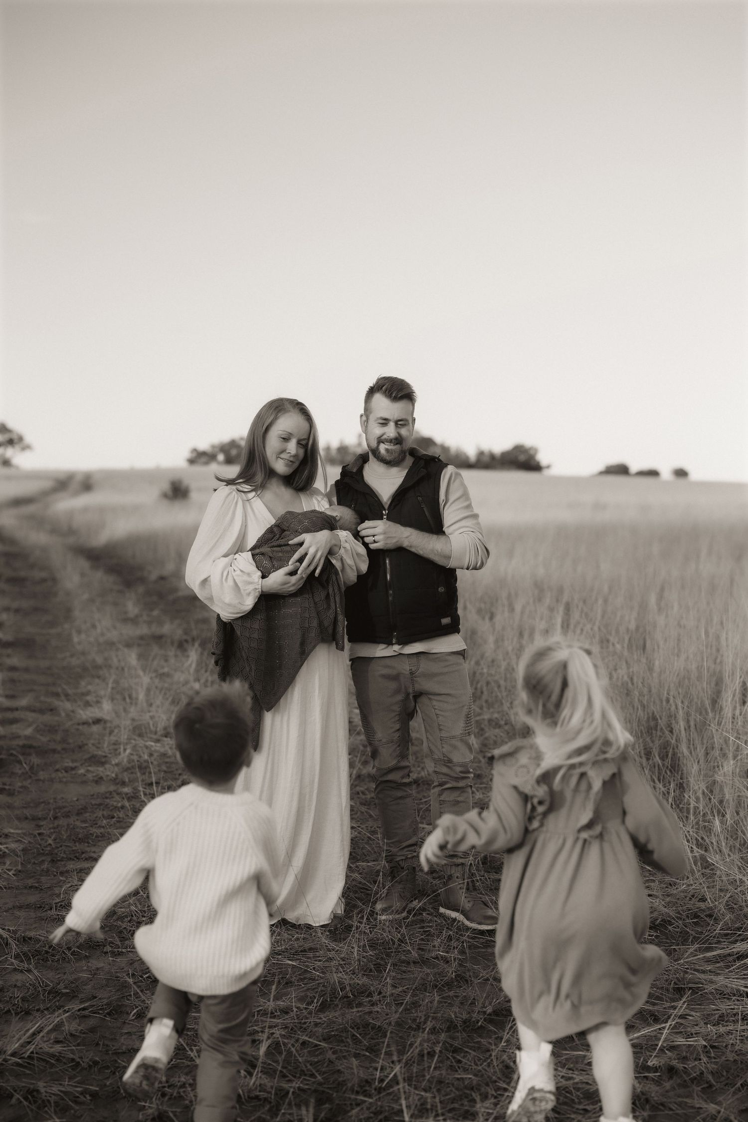 Black and white family portrait in a field with children running in the foreground.